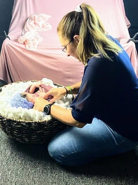Newborn photographer posing sleeping baby in wicker basket during professional studio photo session.