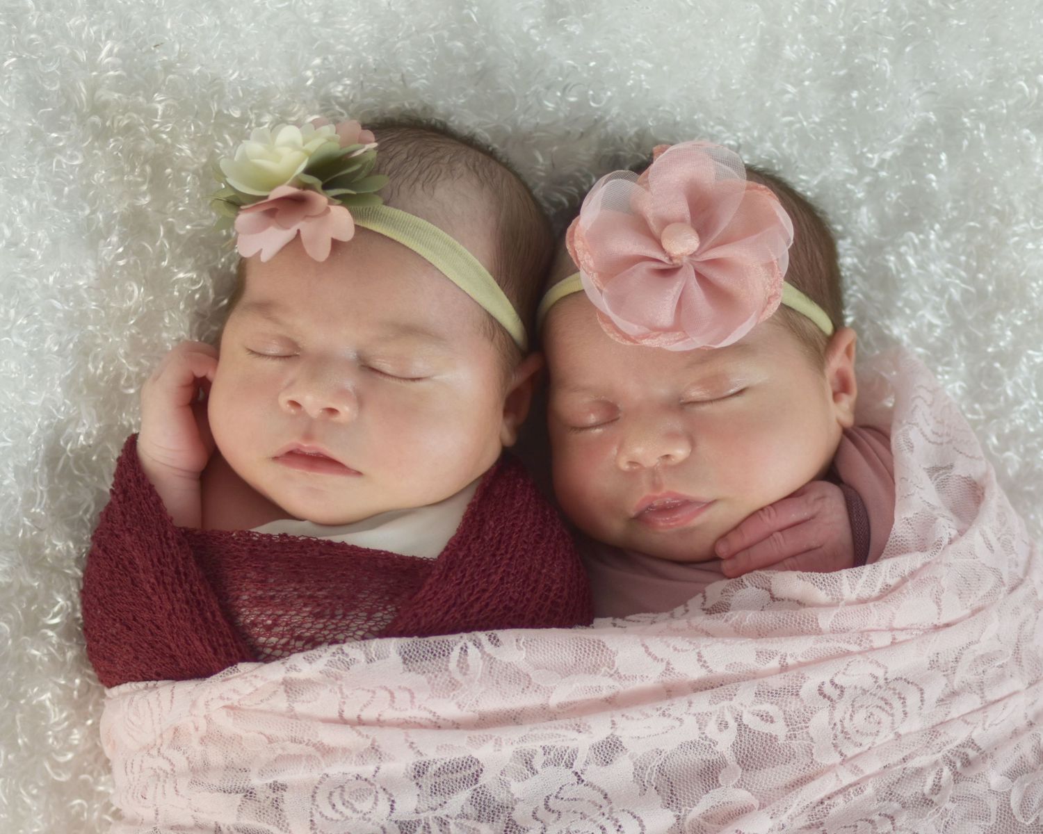 Twin babies in pink outfits sleeping on textured white background wrapped in pink lace fabric, San Antonio newborn photographer