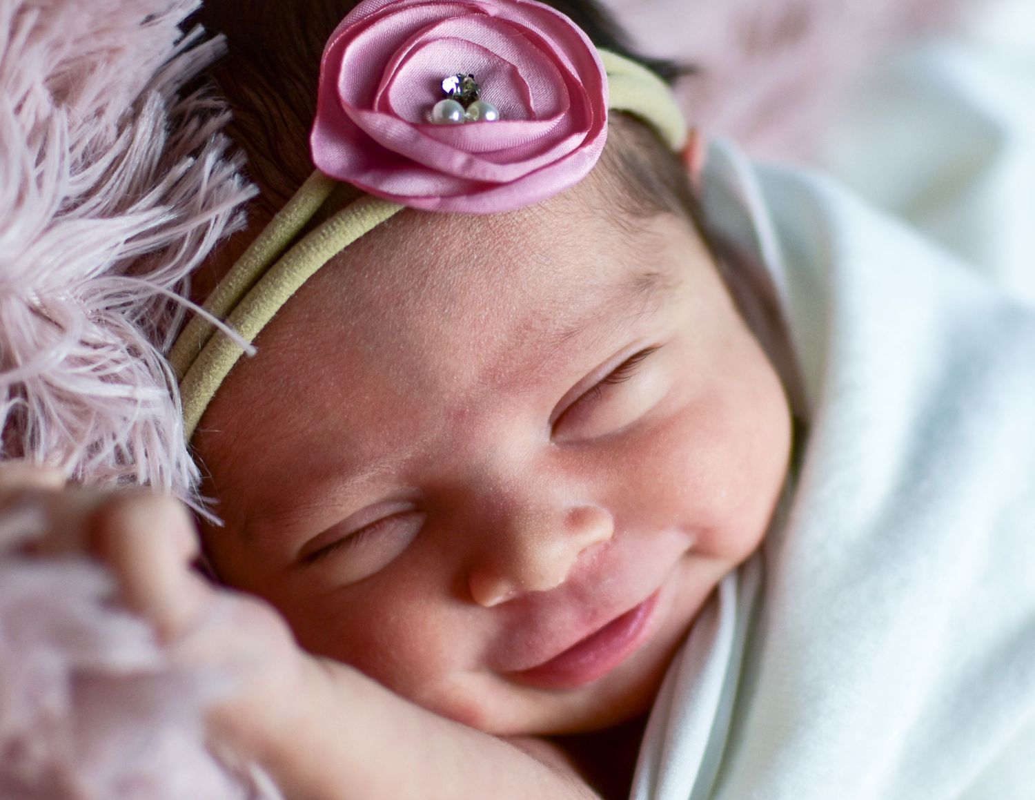 Sleeping newborn baby wrapped in pink blanket with matching pink flower headband smiling, San Antonio newborn photography session