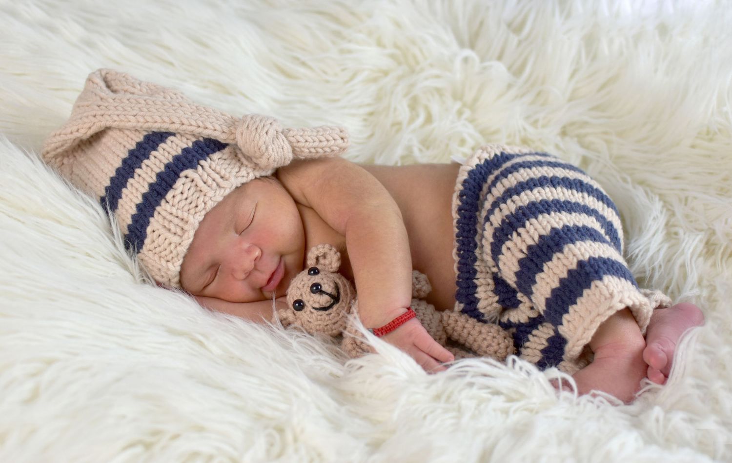 Newborn wearing striped outfit resting peacefully on white fur backdrop. San Antonio newborn photography