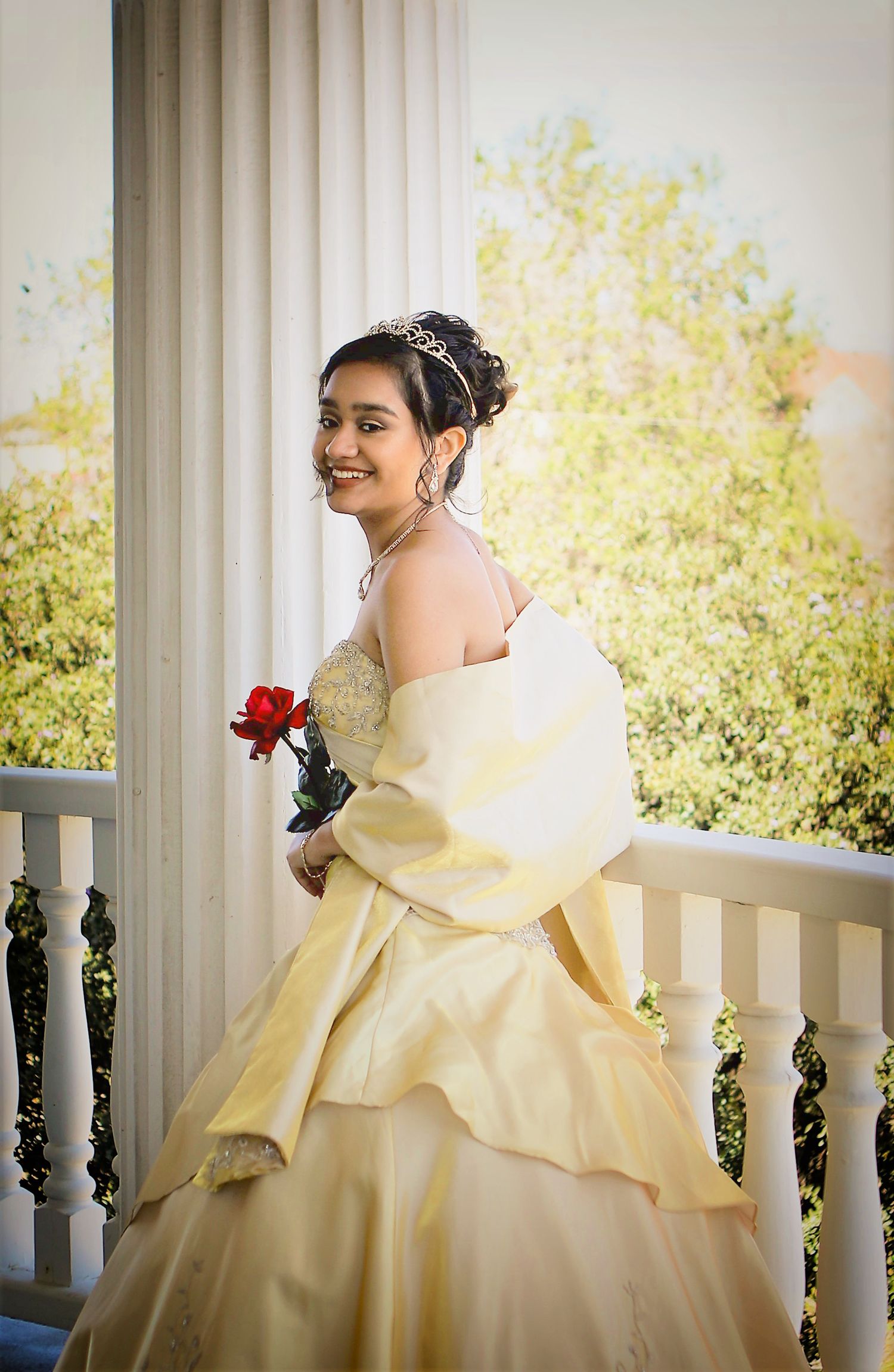 A beautiful sweet 16 in a pale yellow ballgown poses playfully on a white column porch at the Womens Club in San Antonio, Tx sweet 16 photos