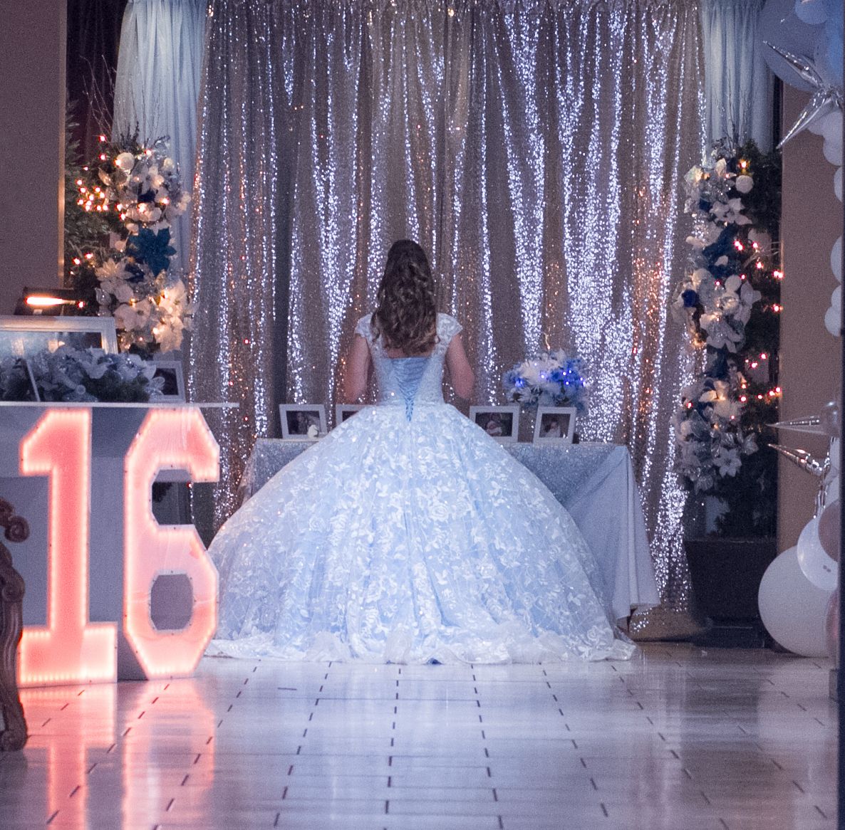 A white sweet 16 dress with a voluminous tulle skirt displayed in an elegant setting with sparkly silver curtains at celebration in San Anto
