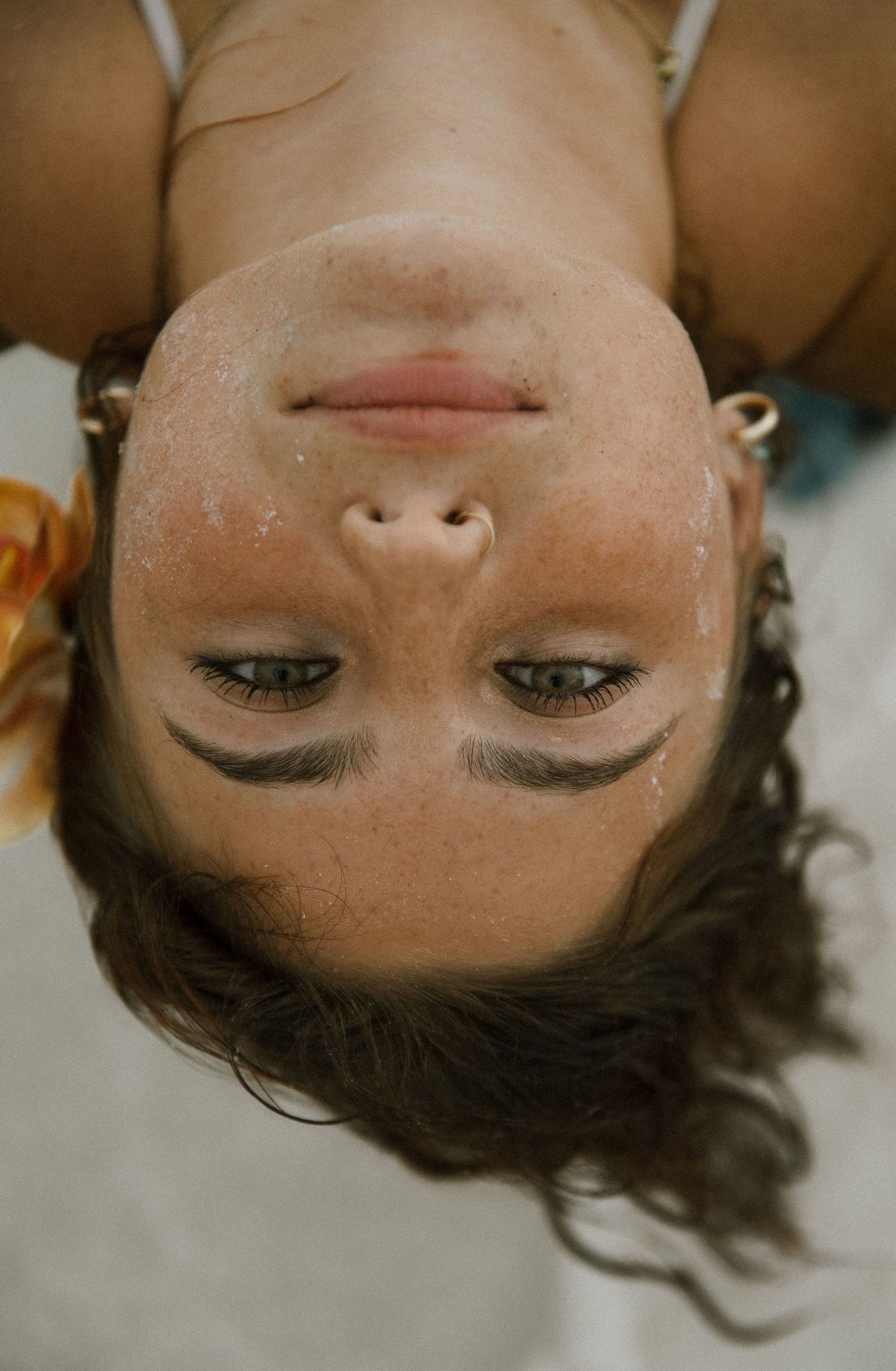 Upside-down close-up portrait of a freckled woman with sandy skin and green eyes lying on a beach.