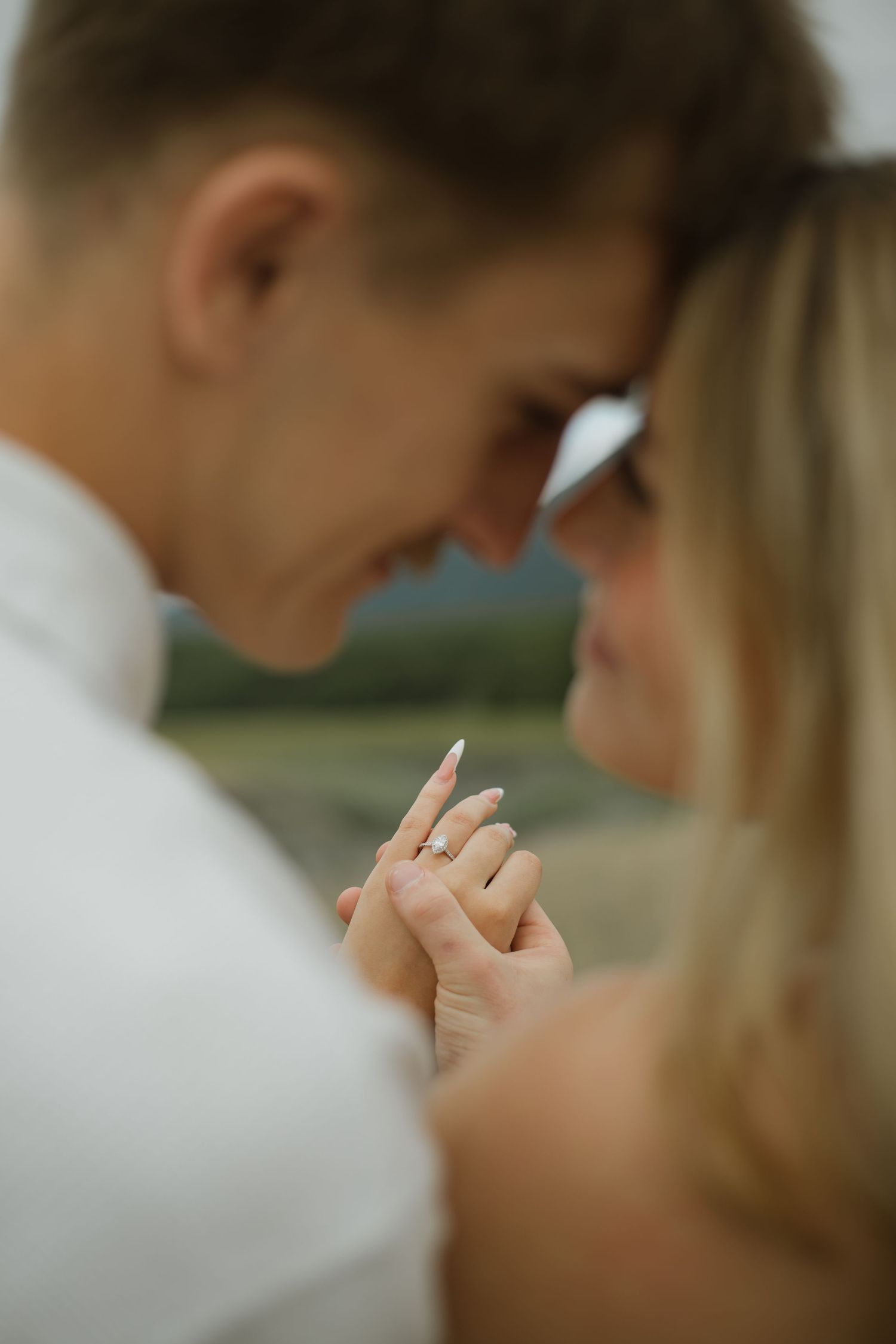 Close-up of a couple touching foreheads as the woman's hand with a diamond engagement ring is held softly.