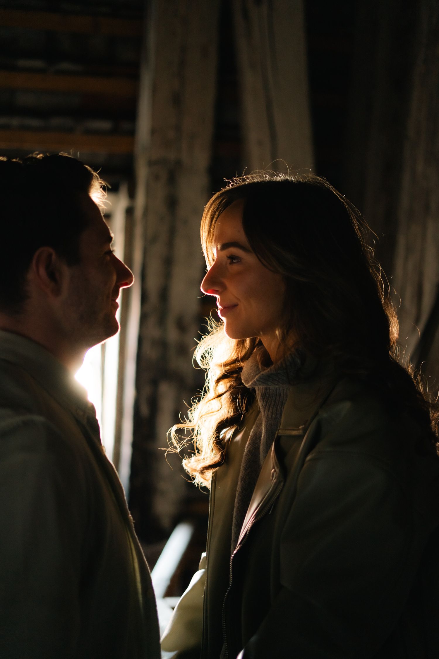 Romantic couple sharing an intimate moment in warm backlit light inside a rustic wooden setting.