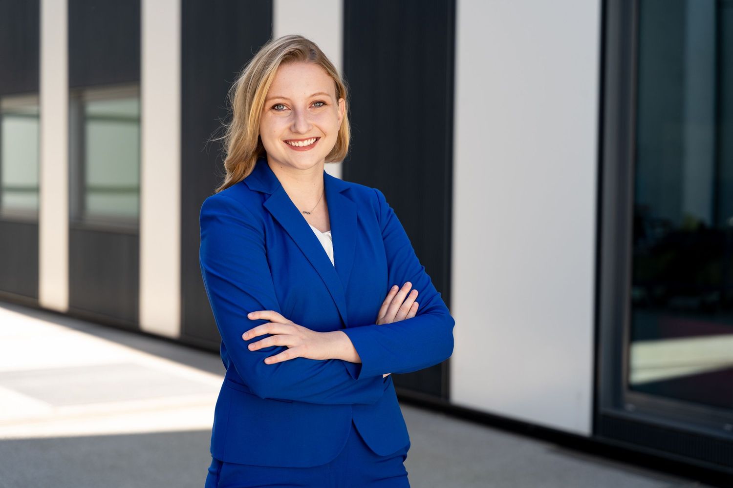 Confident businesswoman in a blue blazer standing with arms crossed outdoors, smiling at the camera.