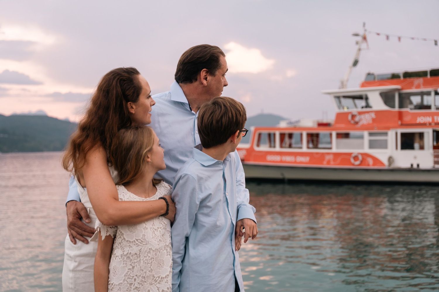 Family of four embracing while watching sunset over water near a ferry boat.