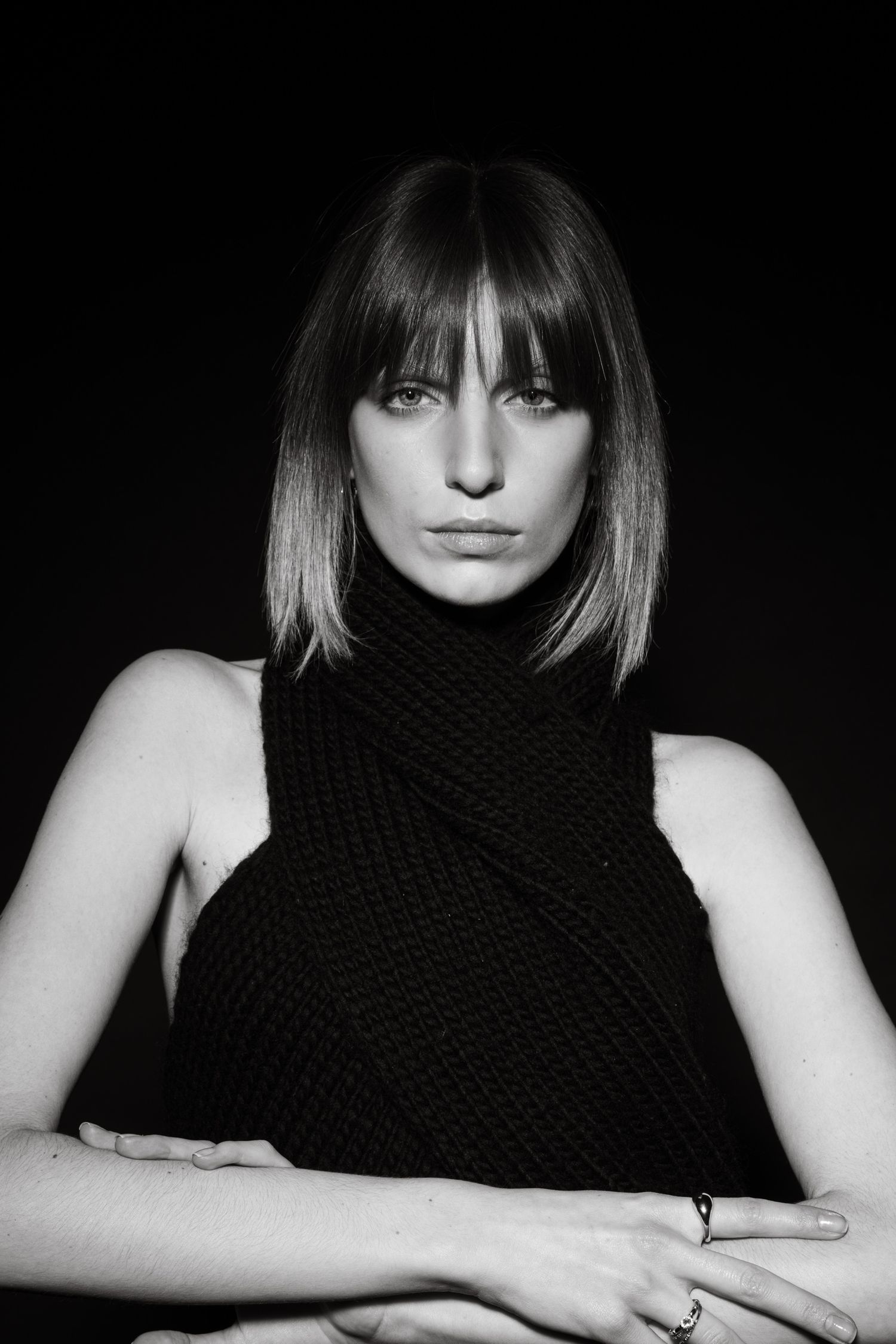 Black and white portrait of a woman with bob haircut wearing a black knit scarf crossed over bare shoulders.