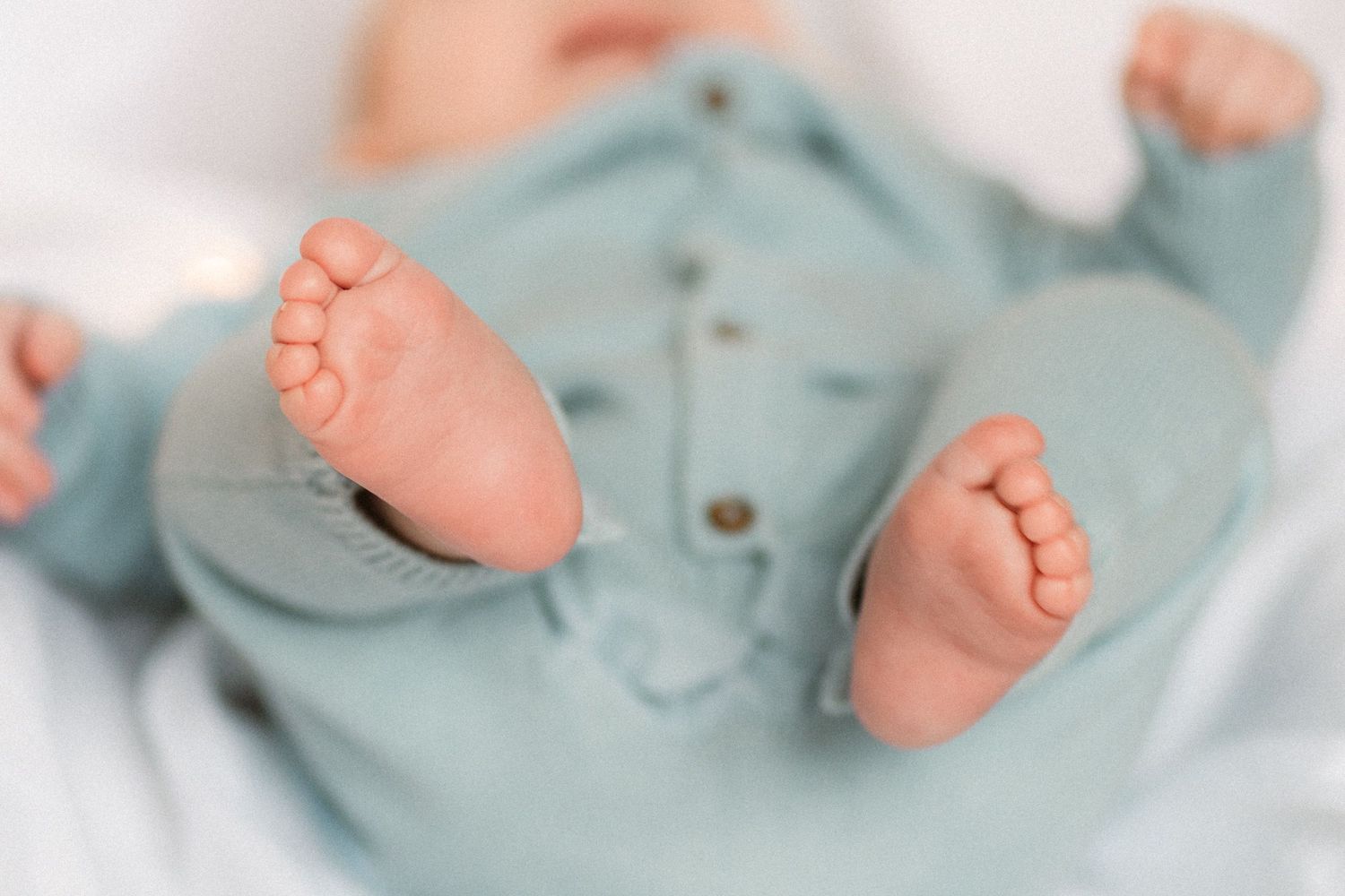 Close-up of tiny newborn baby feet in a soft teal knit onesie.