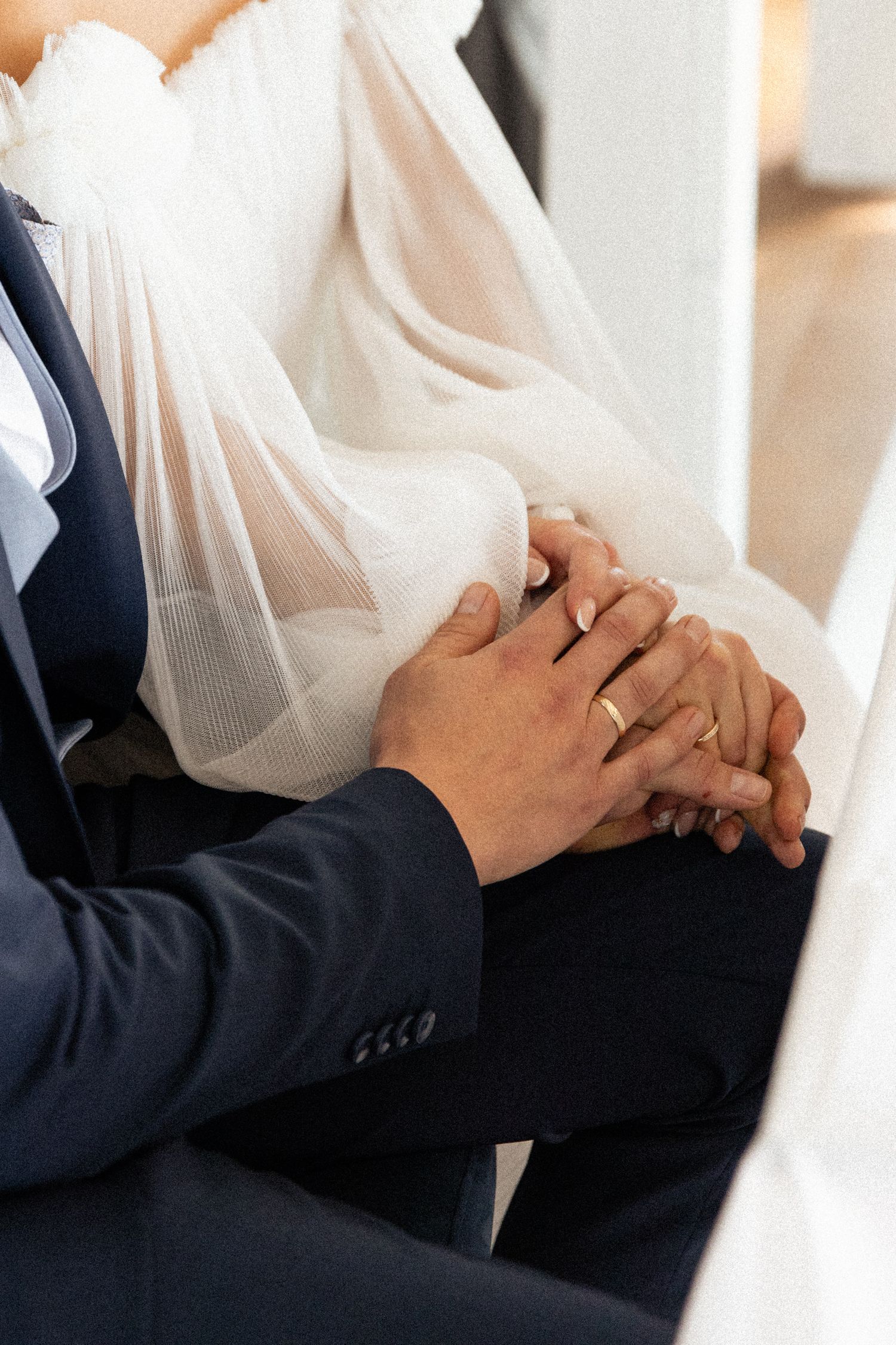 Close-up of newlyweds holding hands with wedding rings visible during intimate wedding ceremony.
