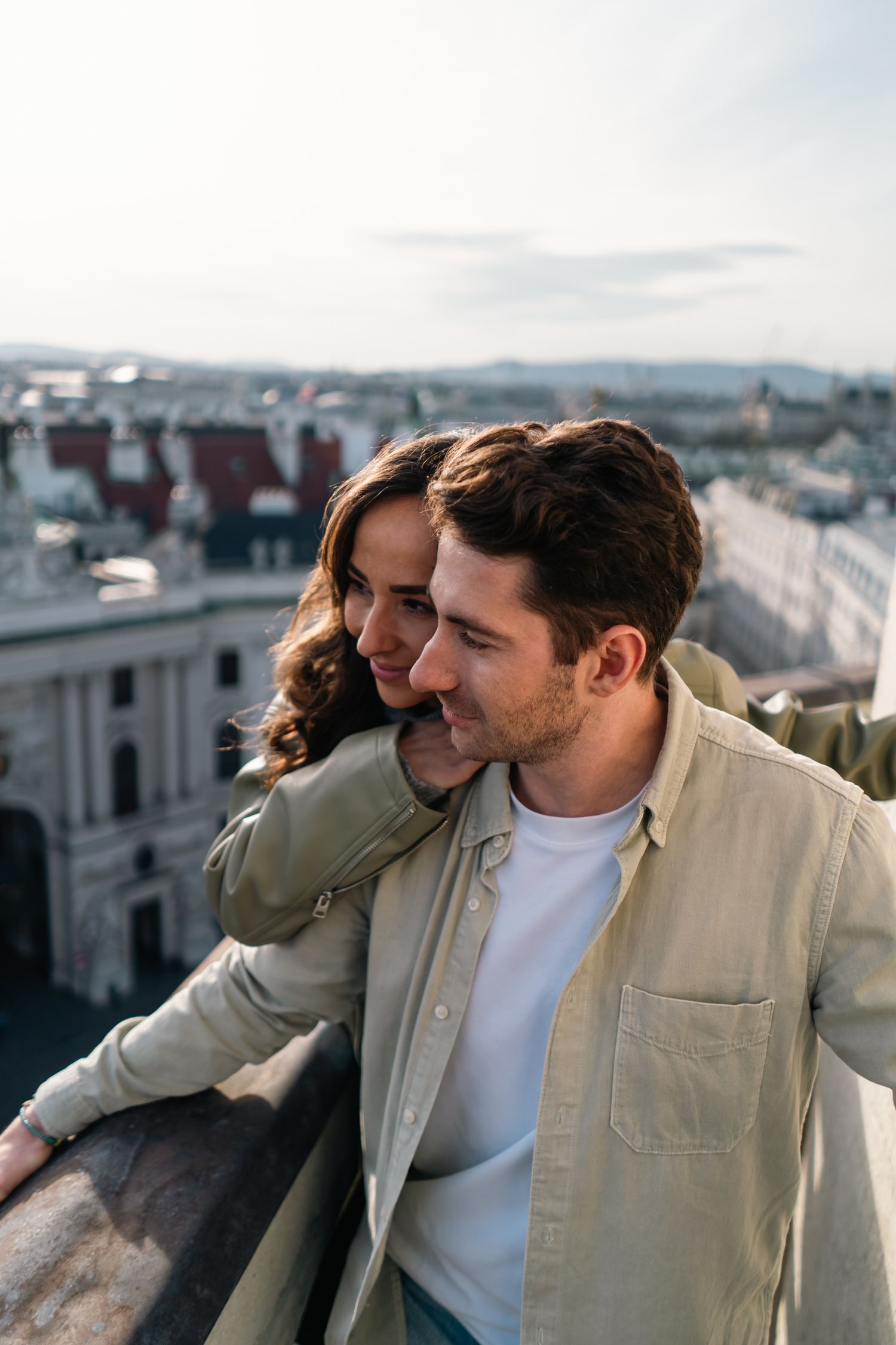 Romantic couple on rooftop overlooking Vienna cityscape at golden hour sunset.