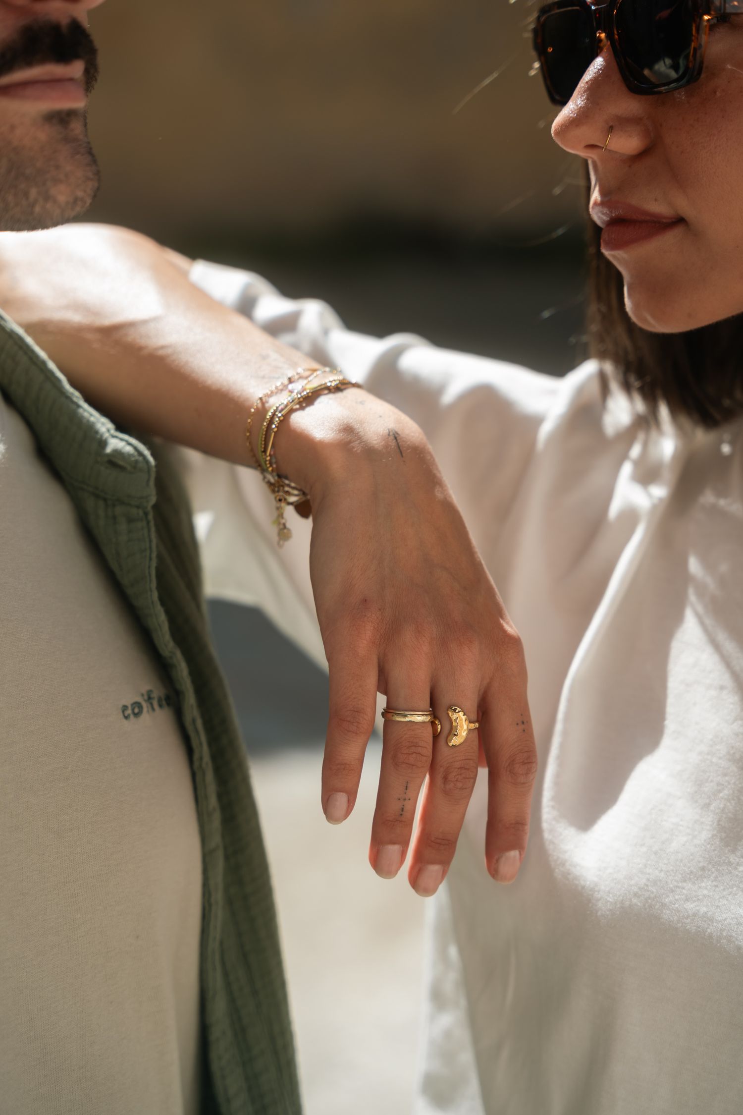 Close-up of a woman's hand adorned with gold rings and bracelets resting on a man's green shirt.