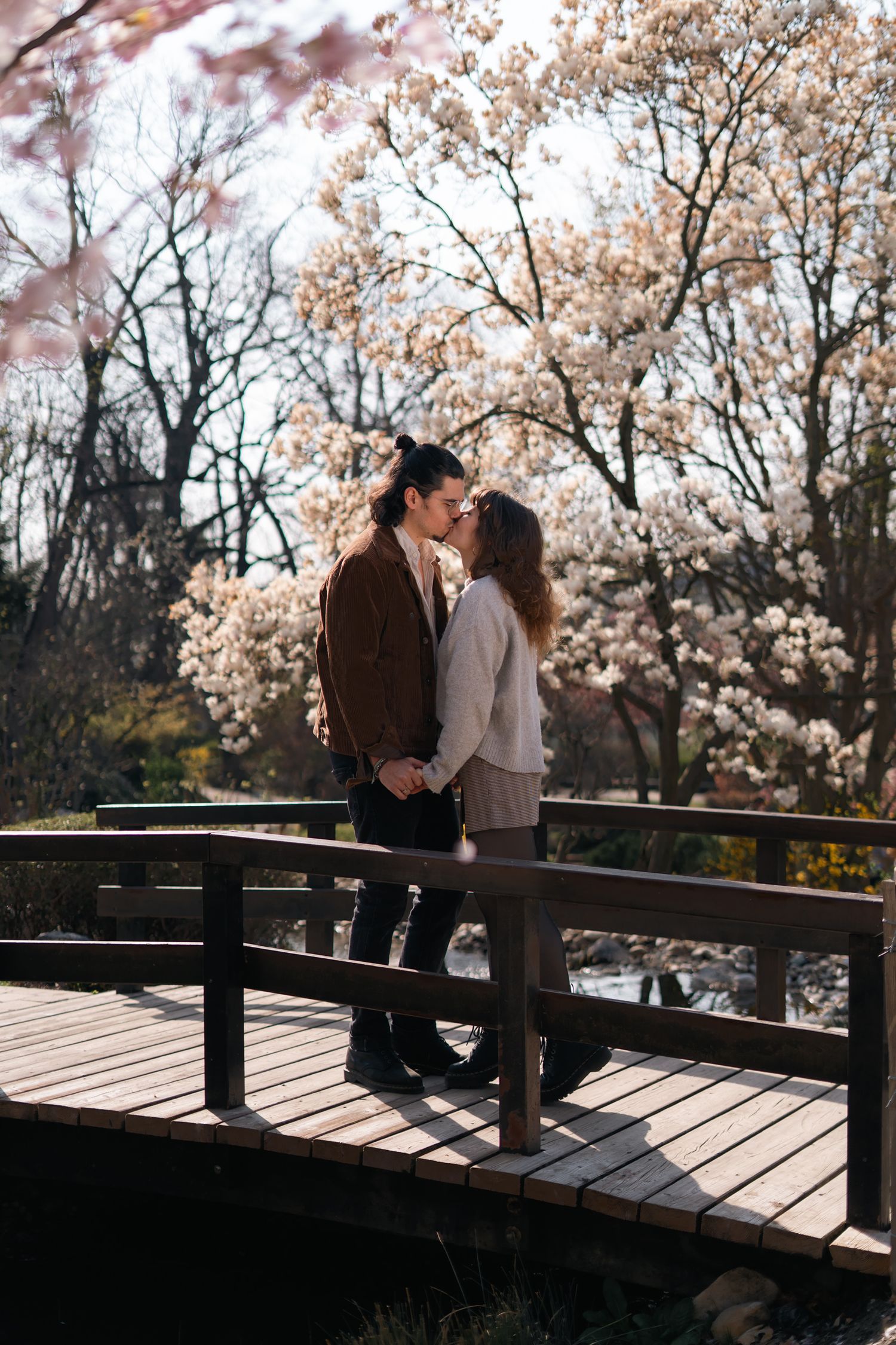 Romantic couple about to kiss on wooden bridge surrounded by blooming magnolia trees in spring.