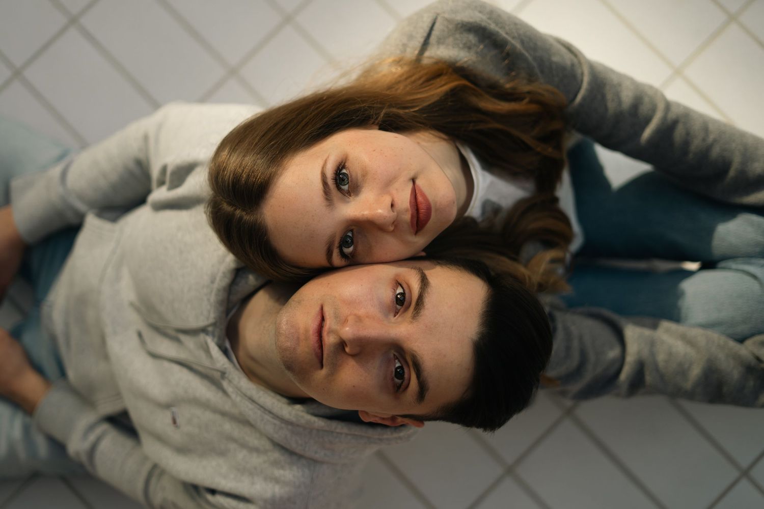 Overhead view of a young couple lying on a tiled floor with heads together looking up.