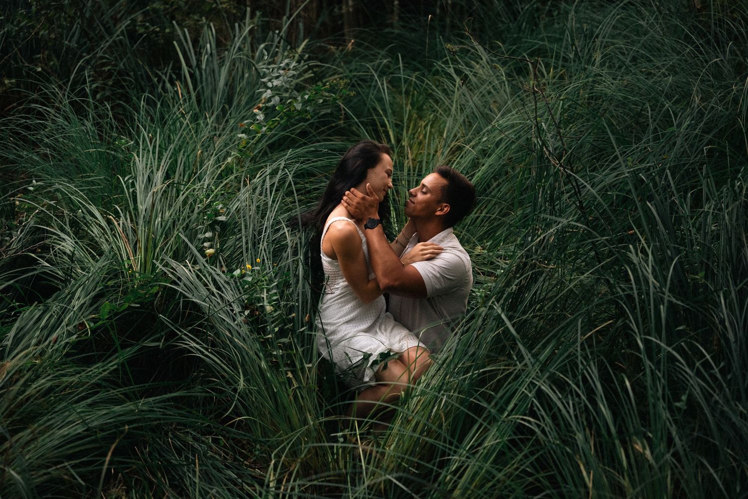 Romantic couple embracing and laughing together in lush green tall grass outdoors.