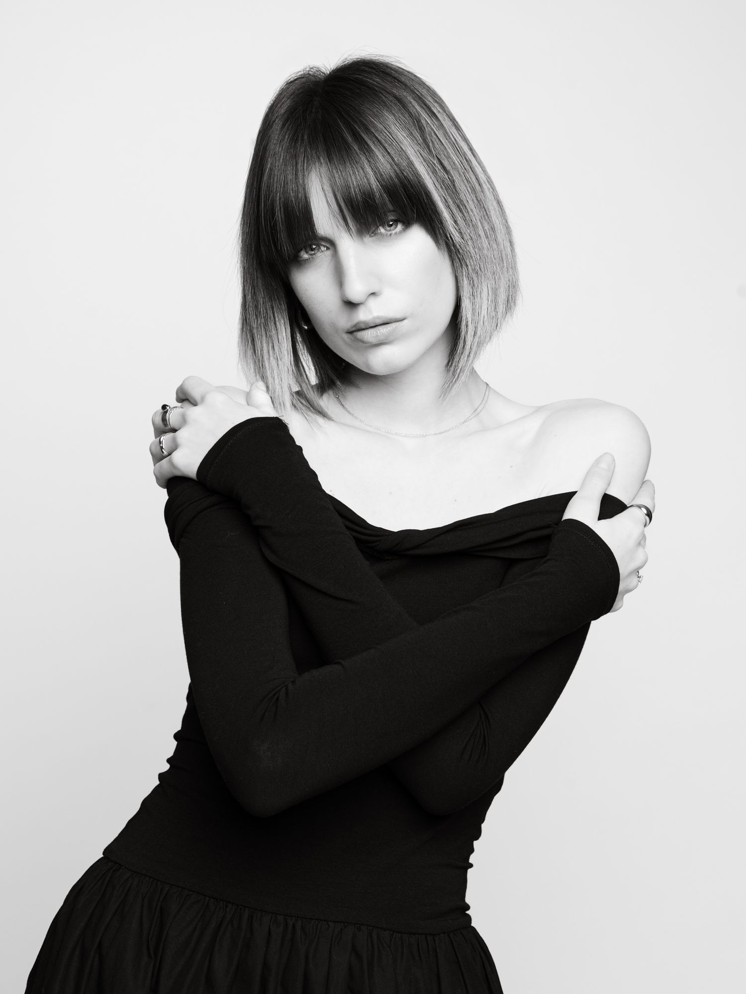 Black and white portrait of a woman with ombre bob and bangs in an off-shoulder black long-sleeve top.