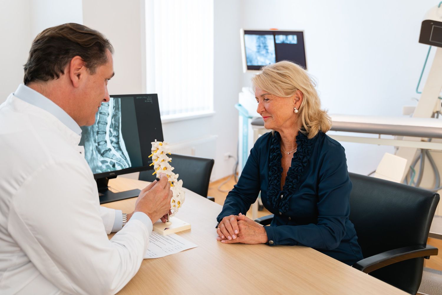 Doctor shows spine model to patient while reviewing X-rays in a clinic.