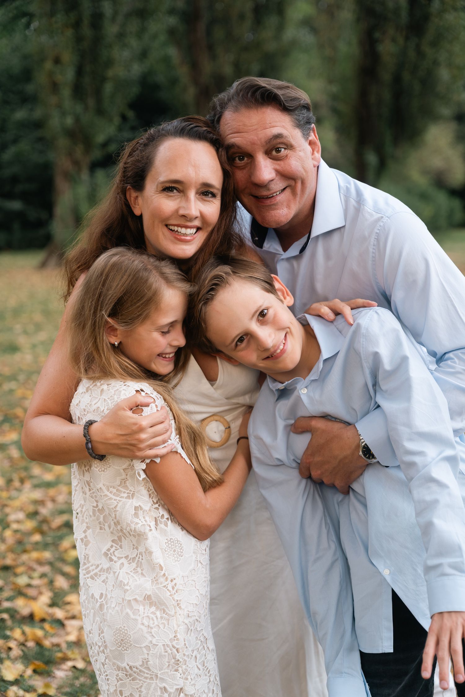 A cheerful family of four shares a loving group hug in an autumn forest setting.