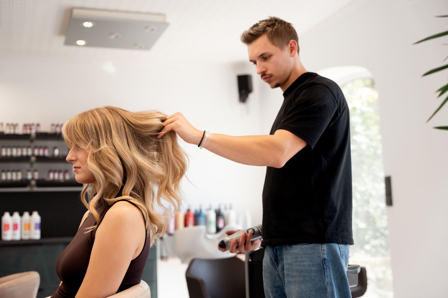 Male hairdresser styling blonde woman's curly hair in modern salon.