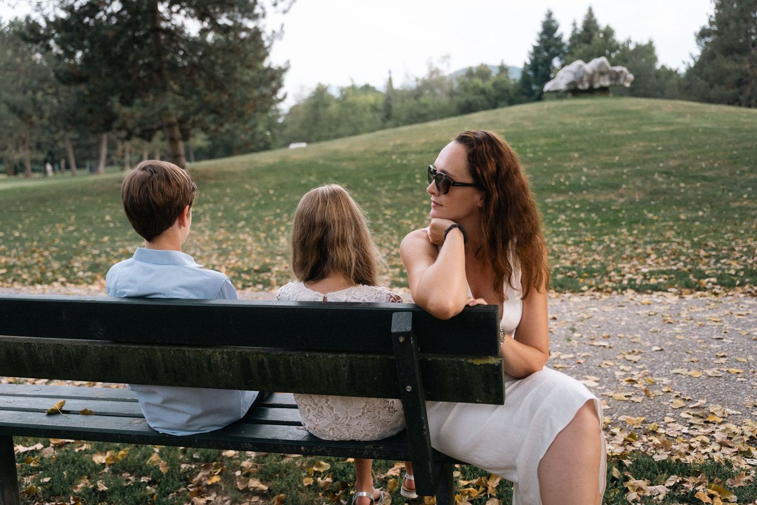 Mother sitting on park bench with two young children on an autumn day.