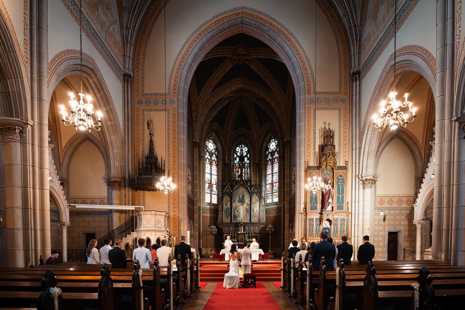 Wide angle view of a wedding ceremony inside a stunning Gothic cathedral with ornate architecture.