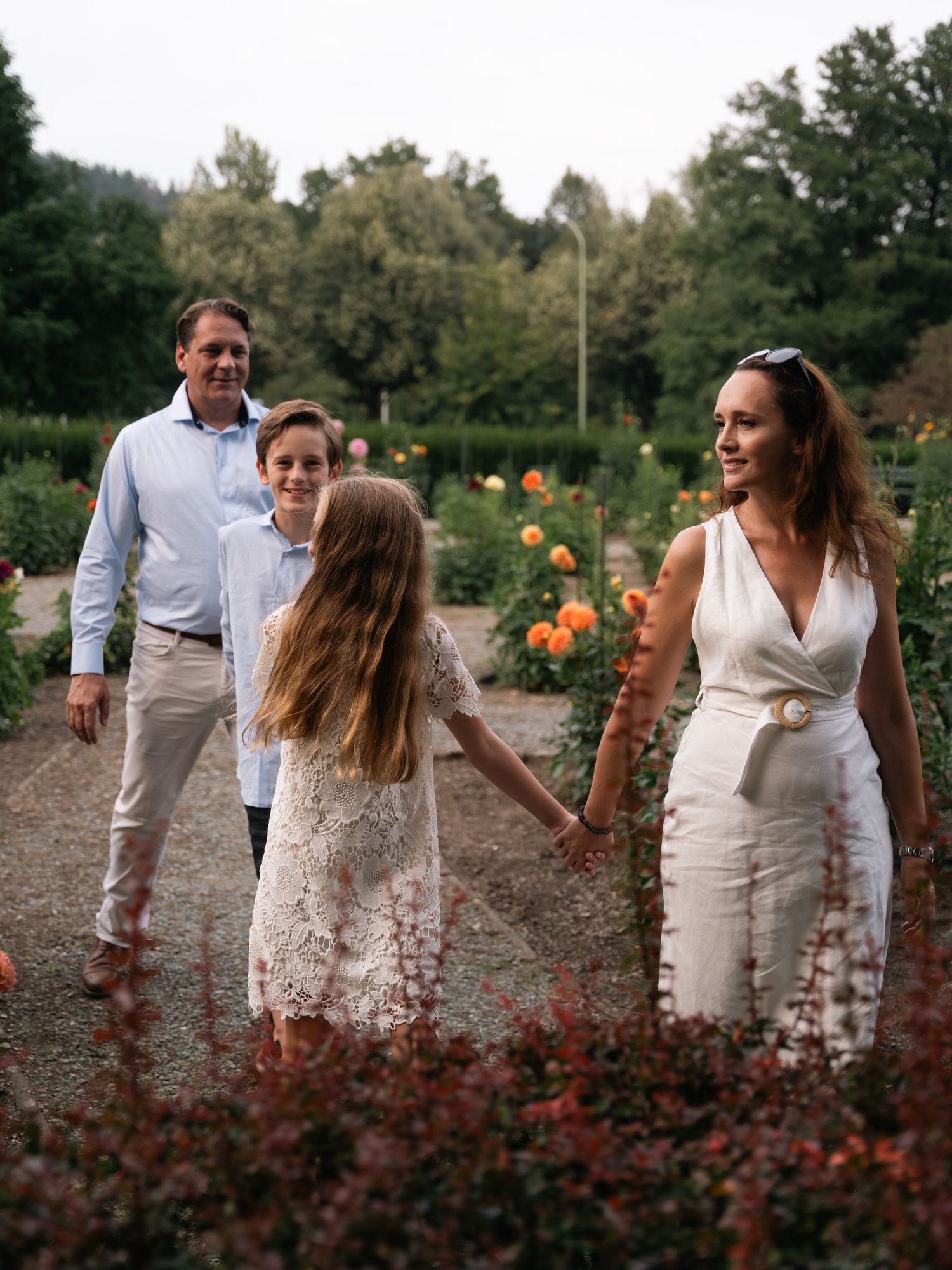 Happy family of four walking through a blooming garden with orange roses at sunset.