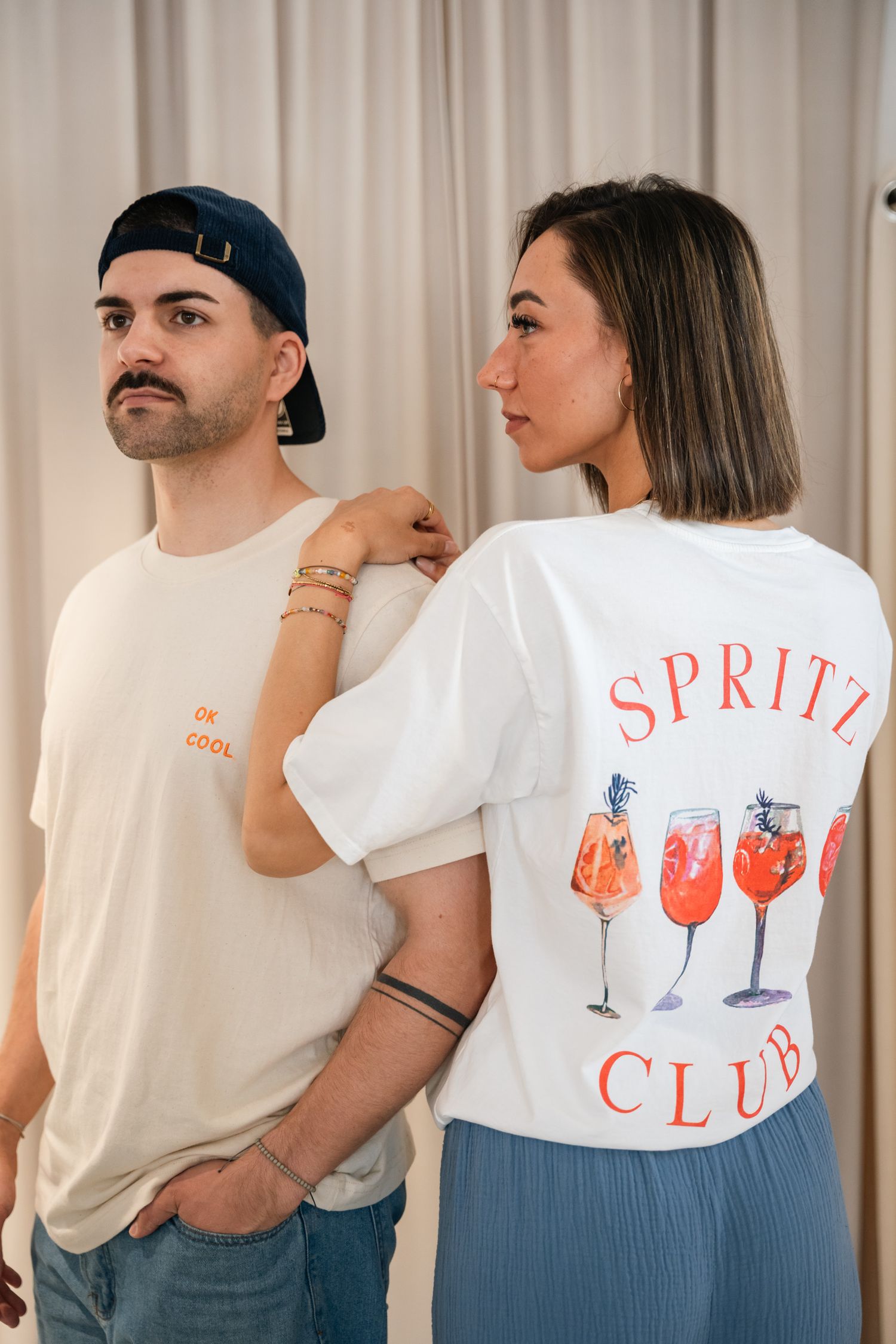 Man and woman wearing Spritz Club graphic t-shirts in a bright studio setting.