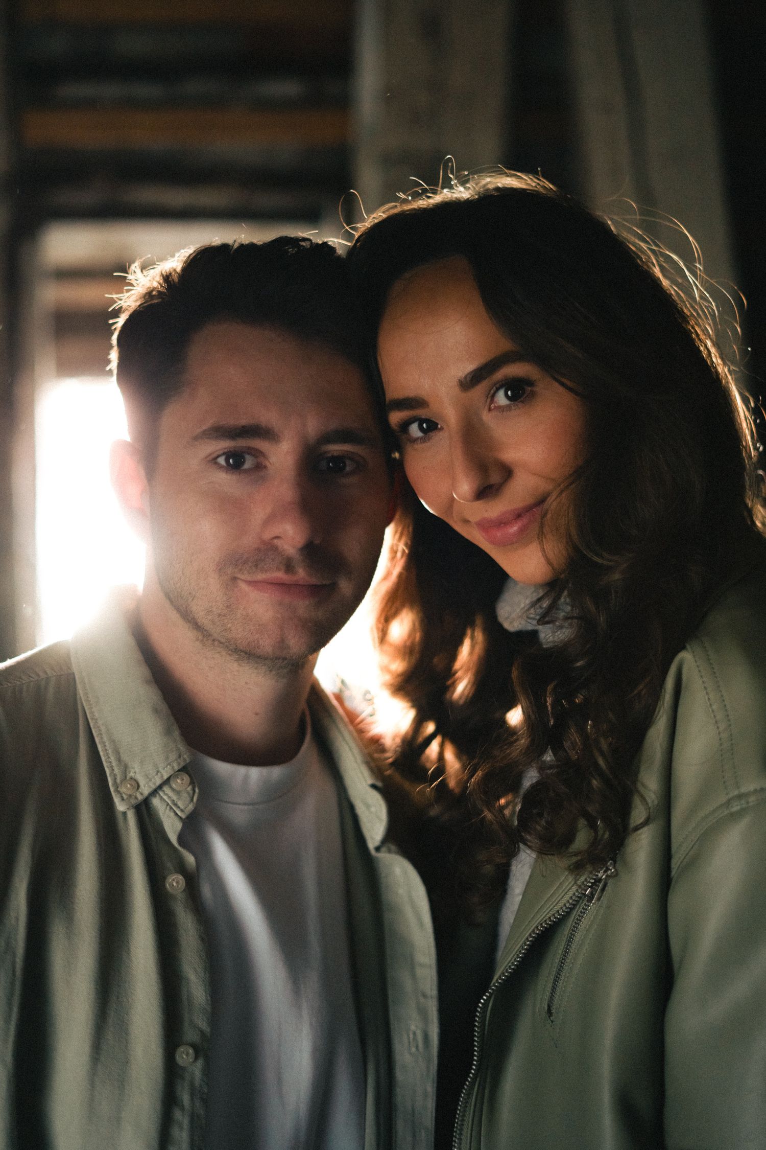 Smiling couple posing together in matching sage green jackets with warm backlit glow.