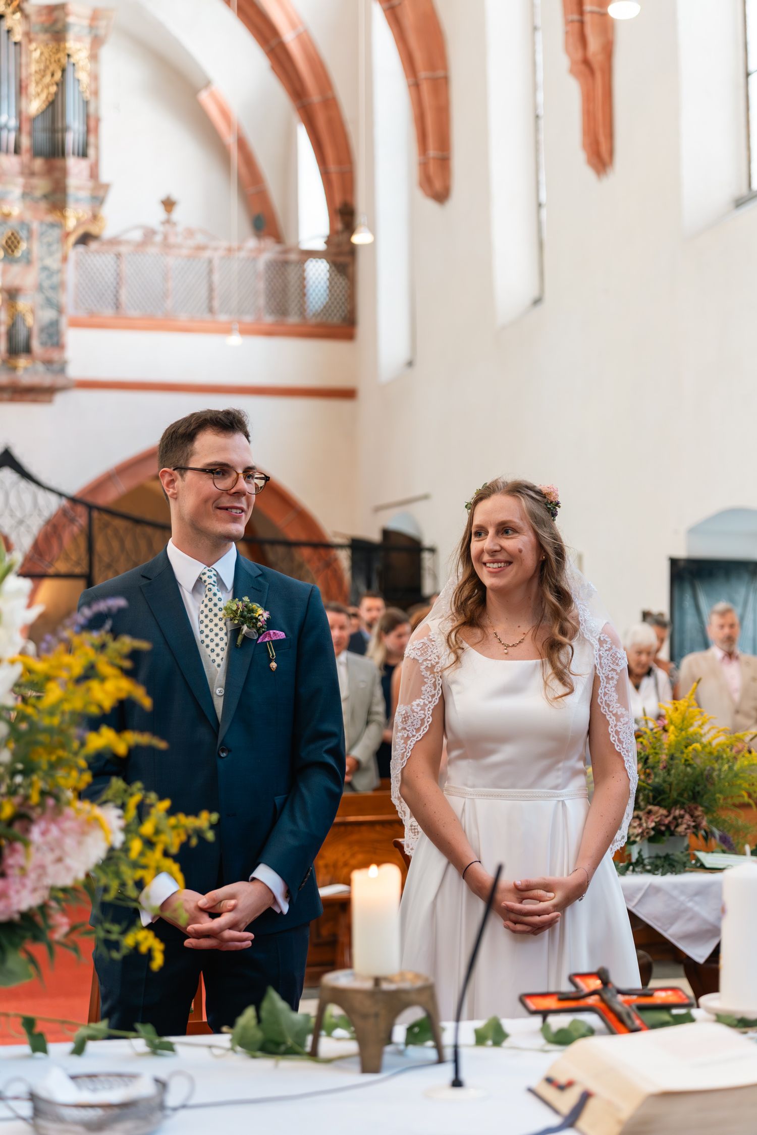 Smiling bride and groom standing at altar during church wedding ceremony with floral arrangements.