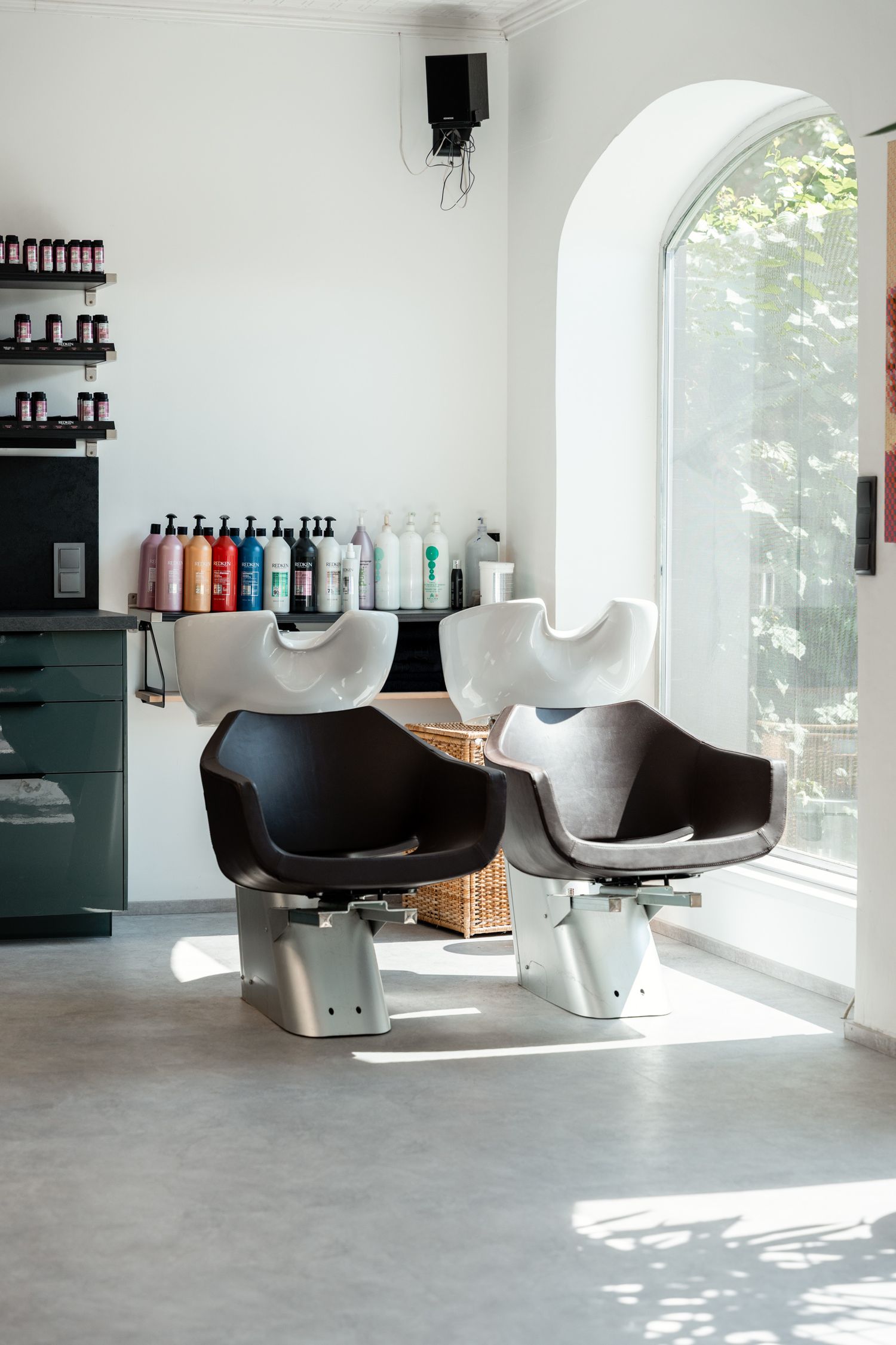 Modern hair salon washing stations with black chairs near arched window.
