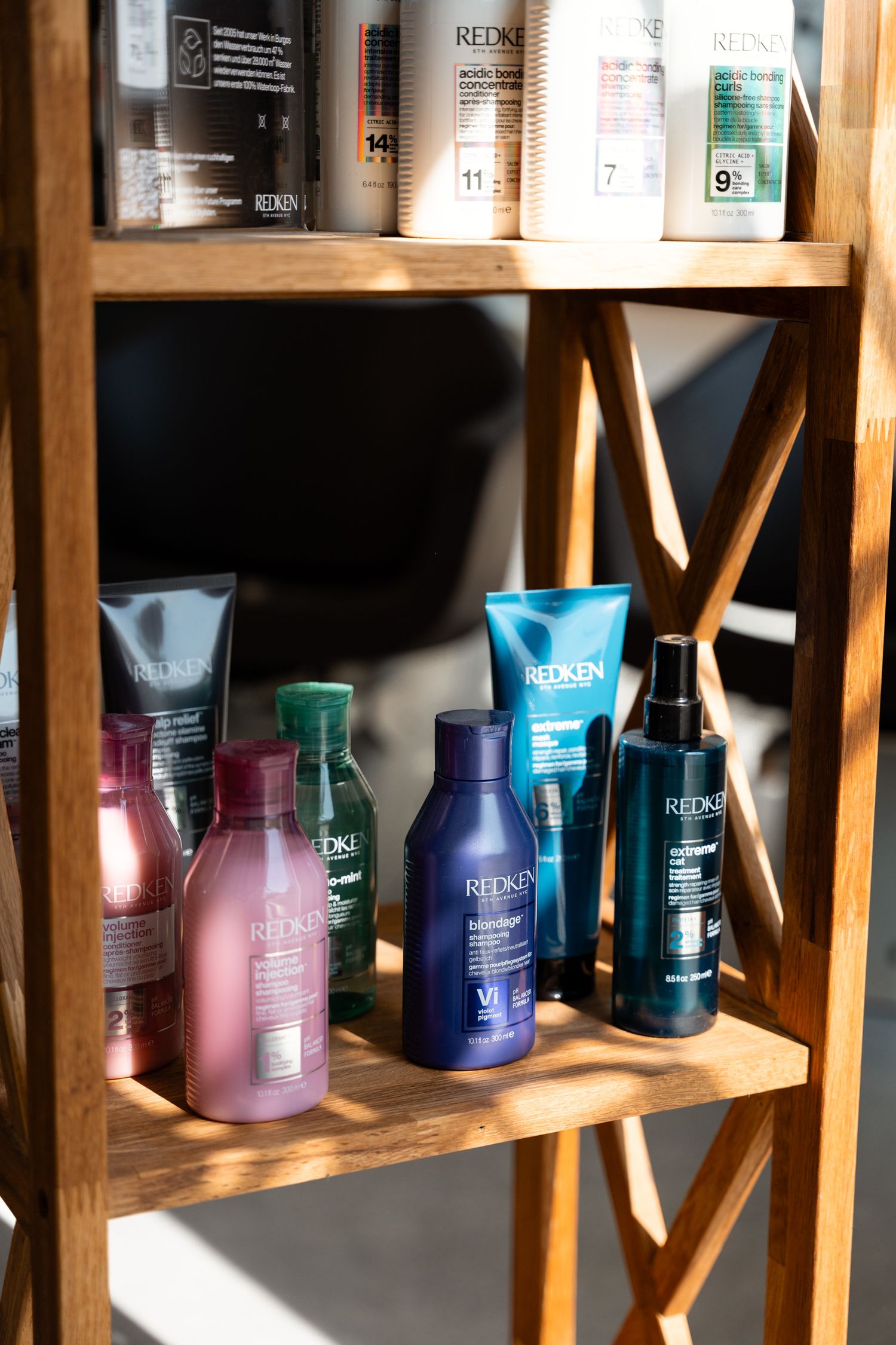 Redken hair care products displayed on a wooden shelf, including shampoos, conditioners, and styling sprays.