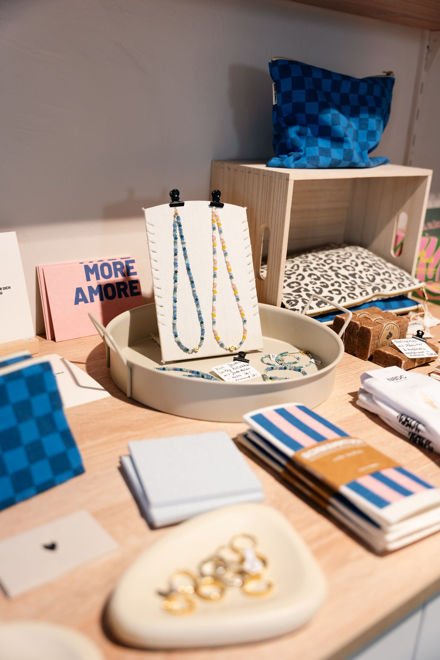 A boutique display table featuring beaded necklaces, gold rings, notebooks, and a More Amore sign.
