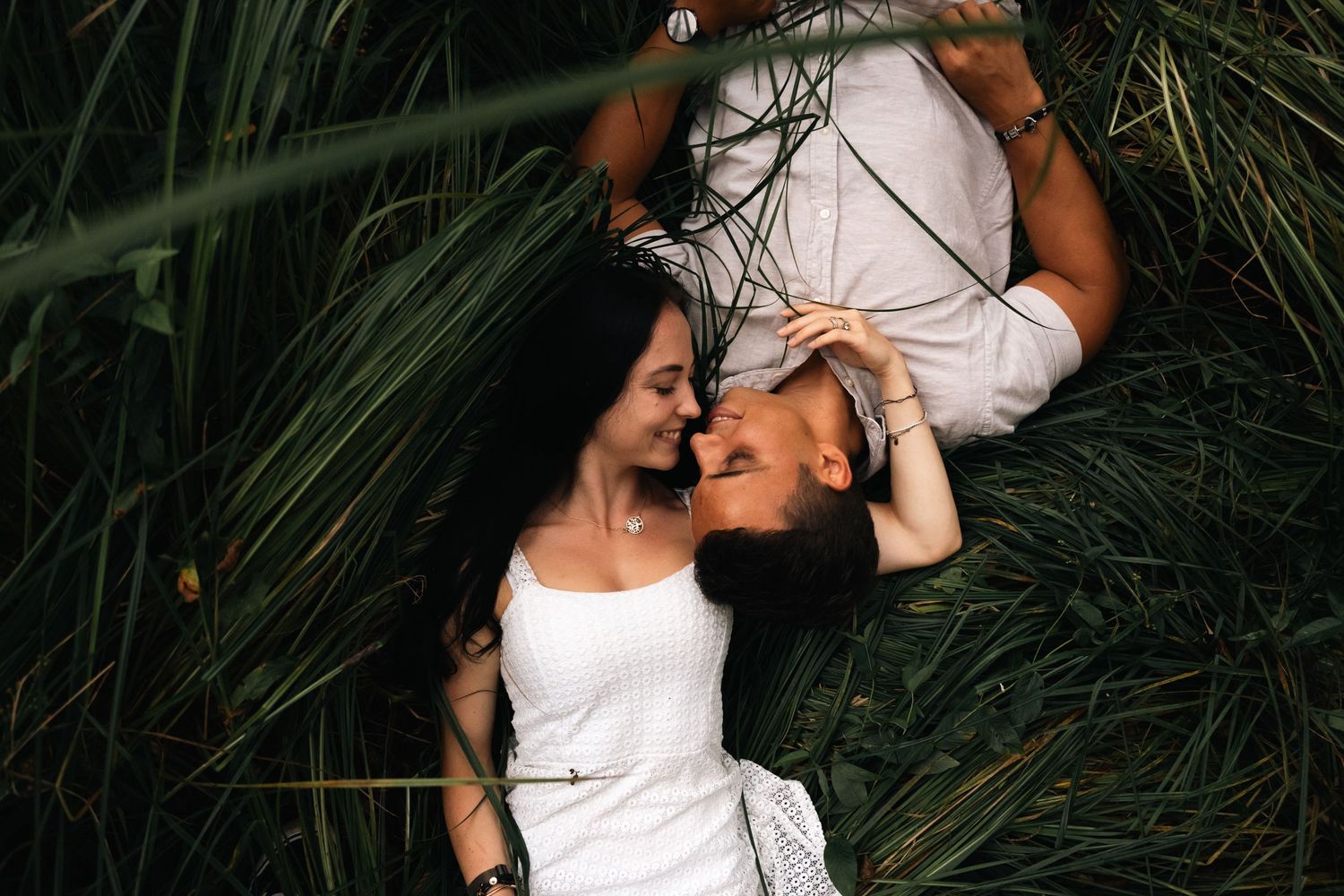 Couple lying in green grass face to face, sharing a tender romantic moment outdoors.