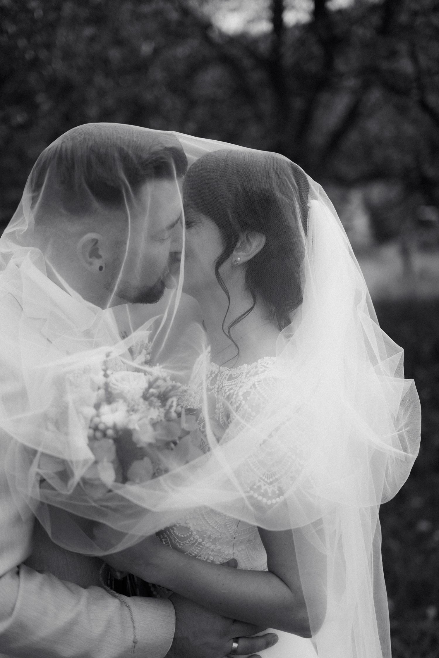 Romantic black and white photo of bride and groom kissing under flowing wedding veil.