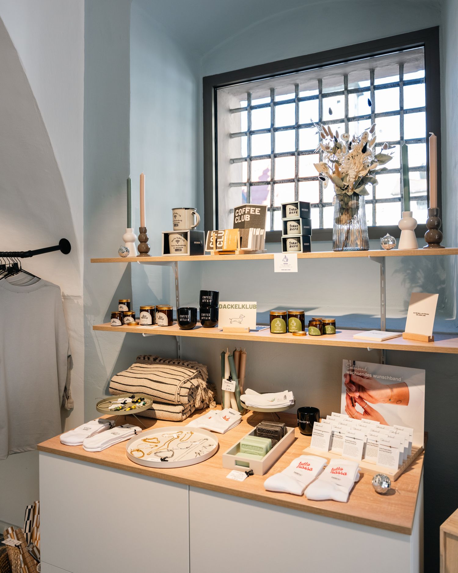A neatly arranged shop shelf with candles, skincare products, folded textiles, and dried flowers.