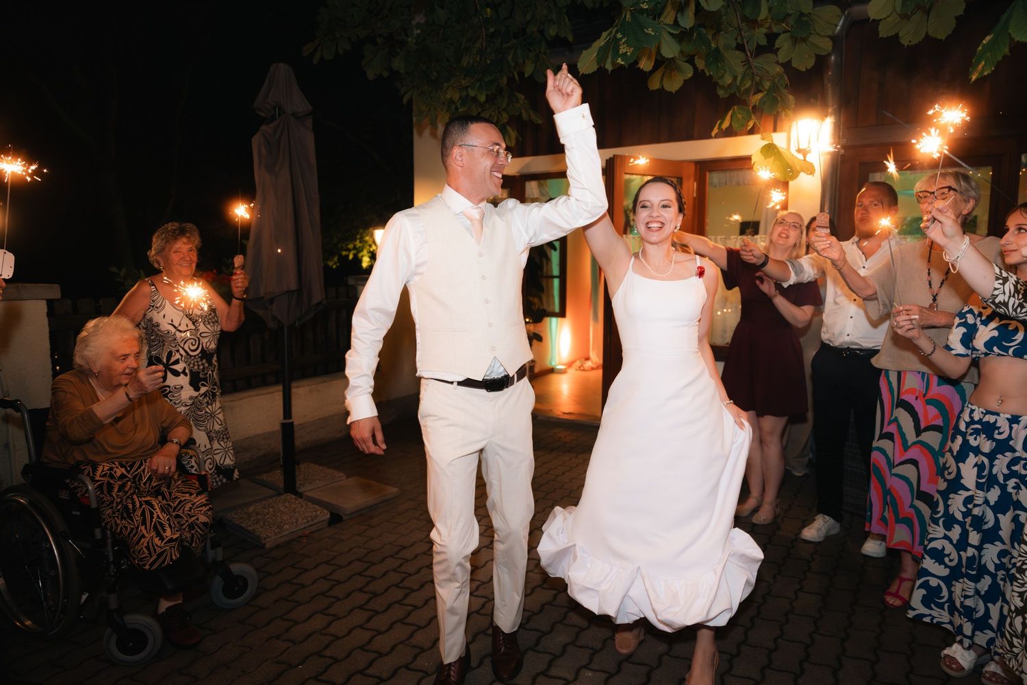 Bride and groom celebrate joyfully with sparklers during evening wedding reception.