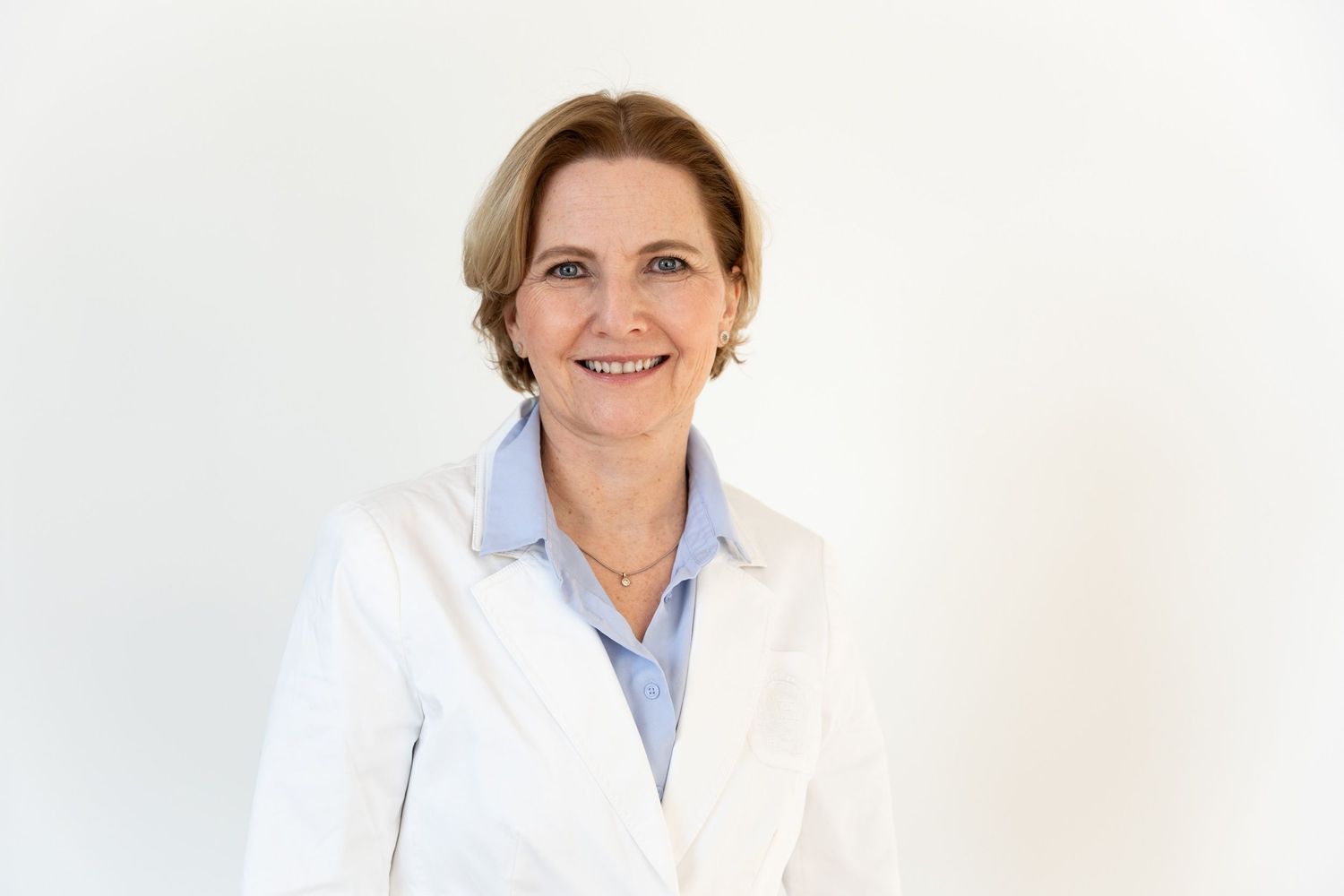 Smiling middle-aged woman in a white lab coat posing against a clean white background.