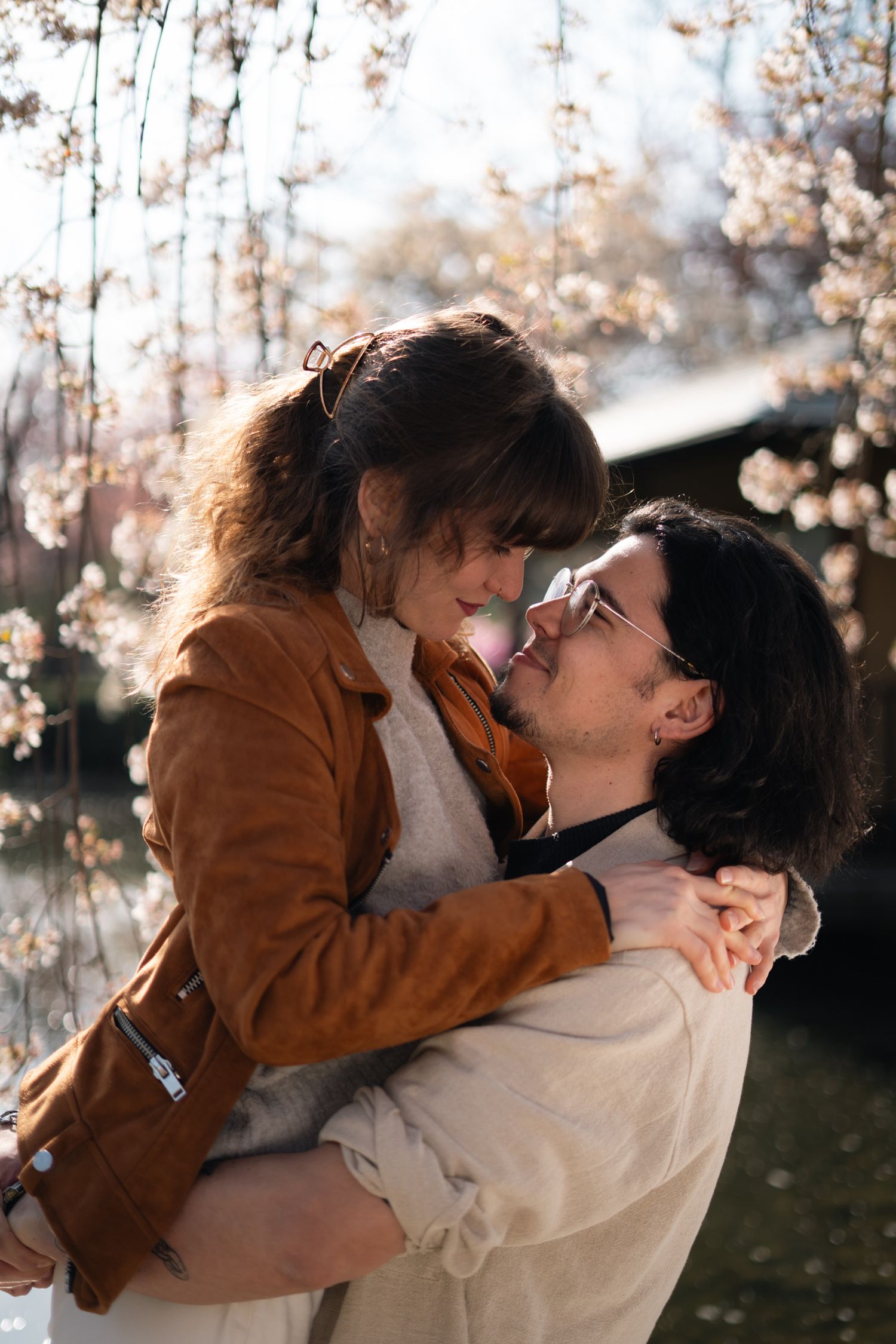 Man lifting woman near blooming cherry blossom trees in romantic spring outdoor setting.