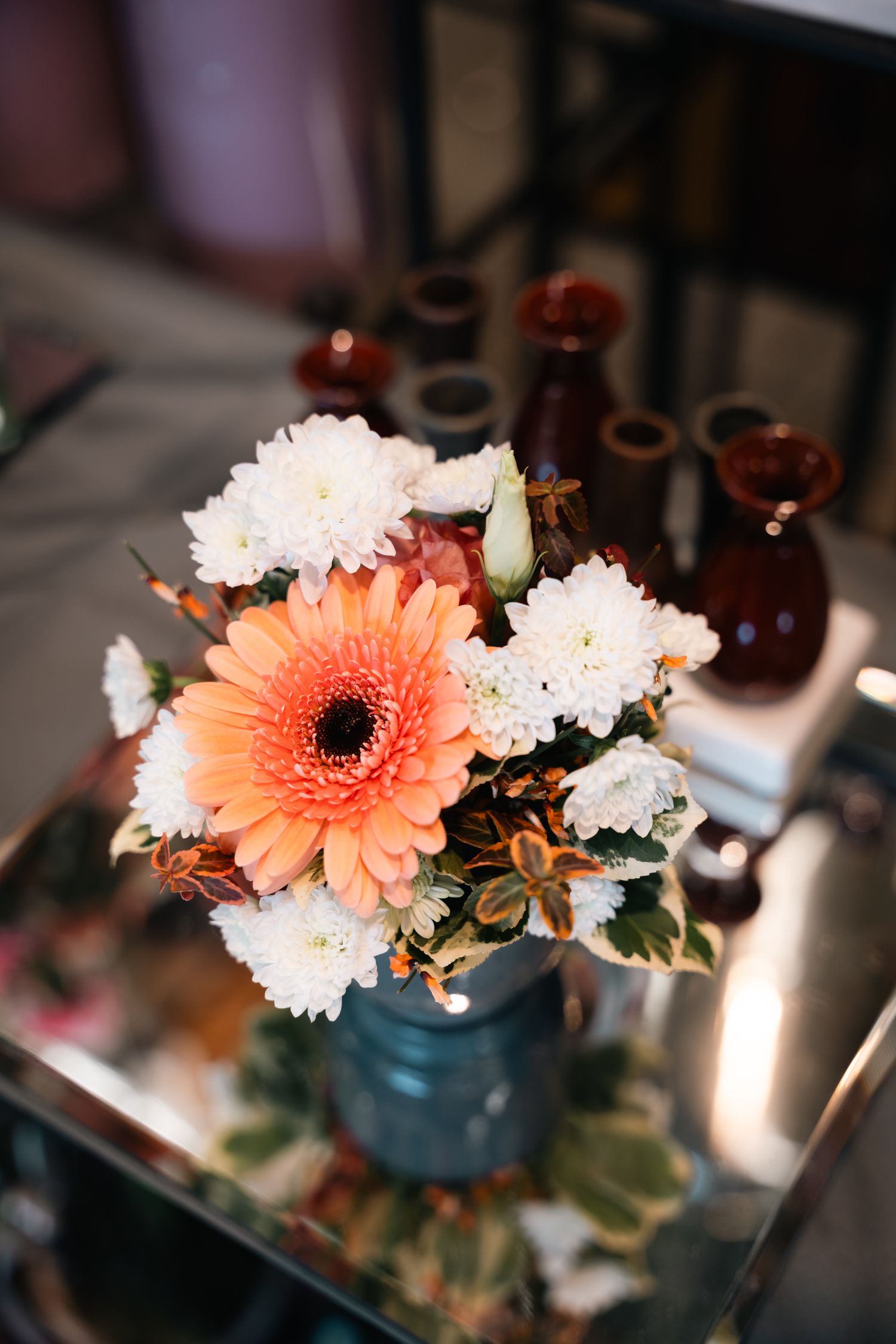 Fresh floral arrangement with orange gerbera daisy and white chrysanthemums on glass table.