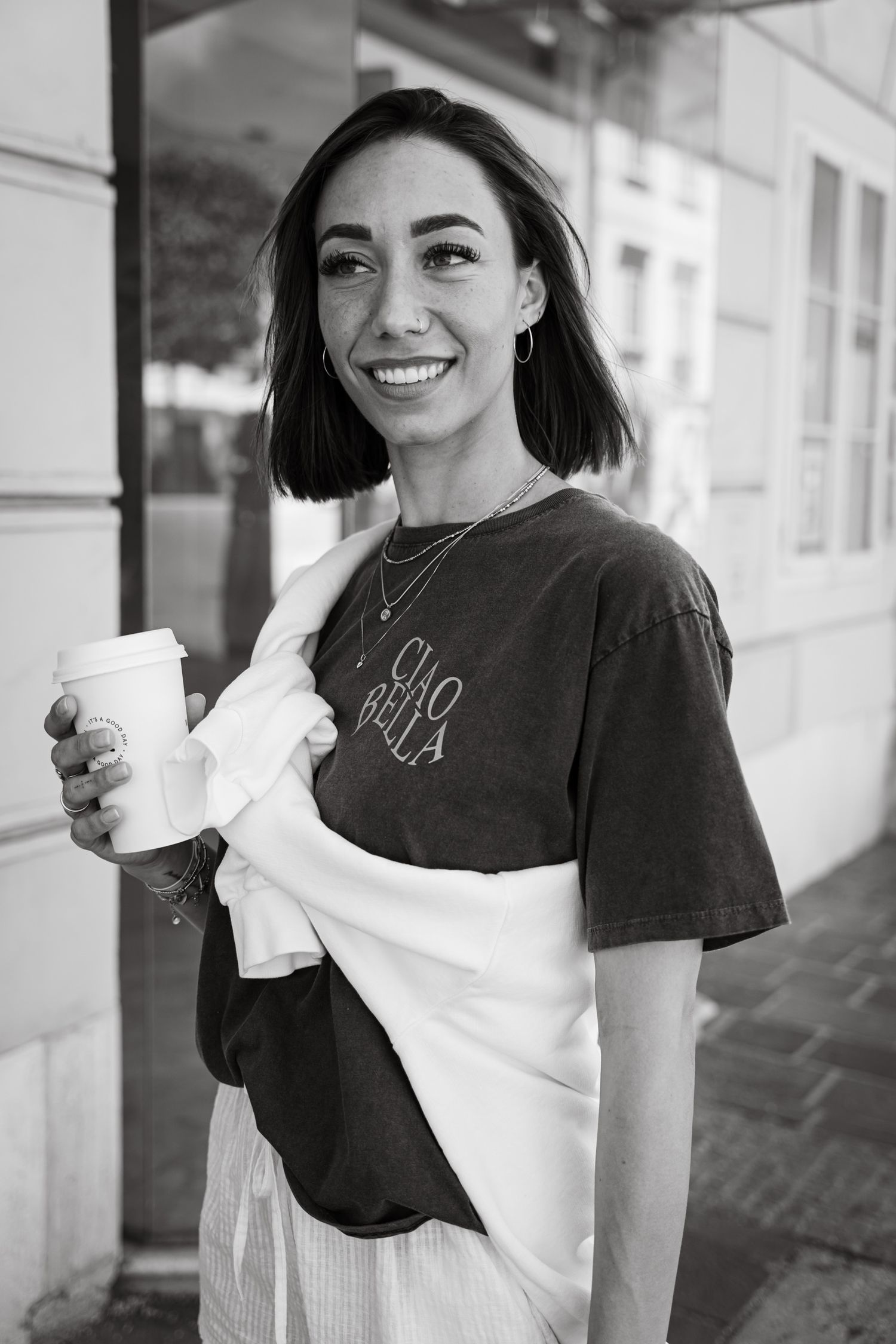 Black and white photo of a smiling woman holding a coffee cup wearing a Ciao Bella graphic tee.