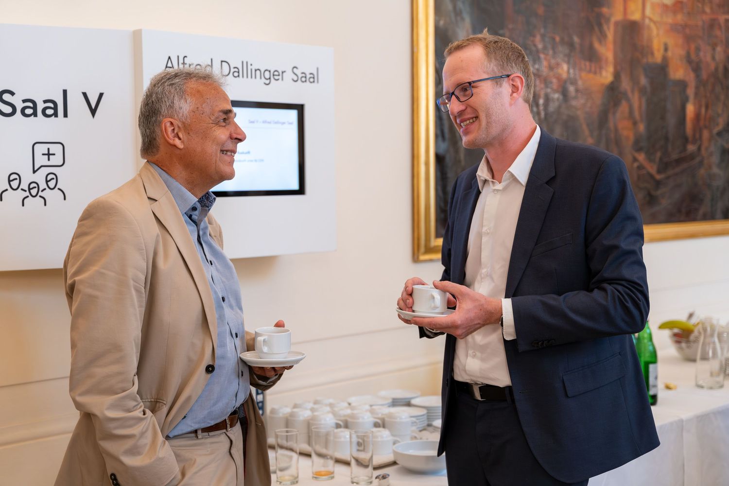 Two men in business attire having a conversation over coffee at a professional networking event.