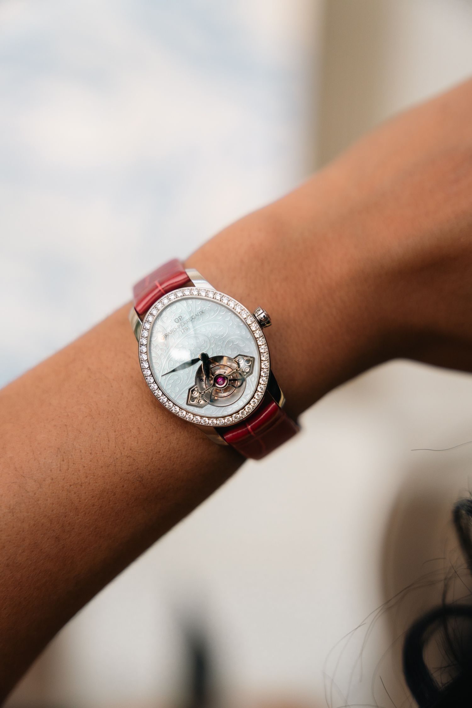 Luxury diamond-bezel watch with blue mother of pearl dial on red leather strap.