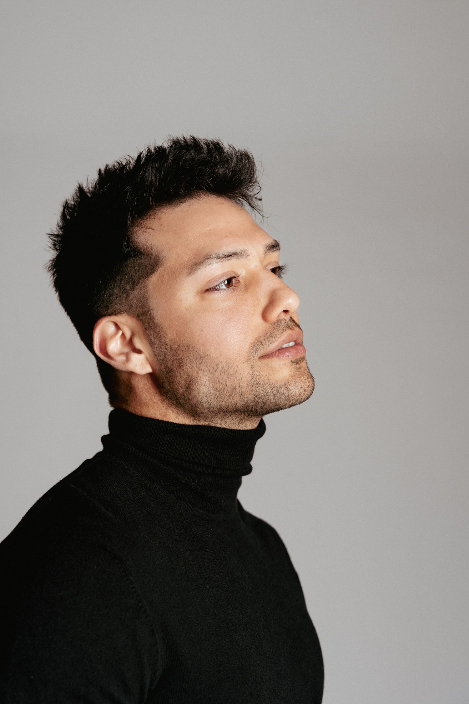 Side profile portrait of man in black turtleneck against gray background.