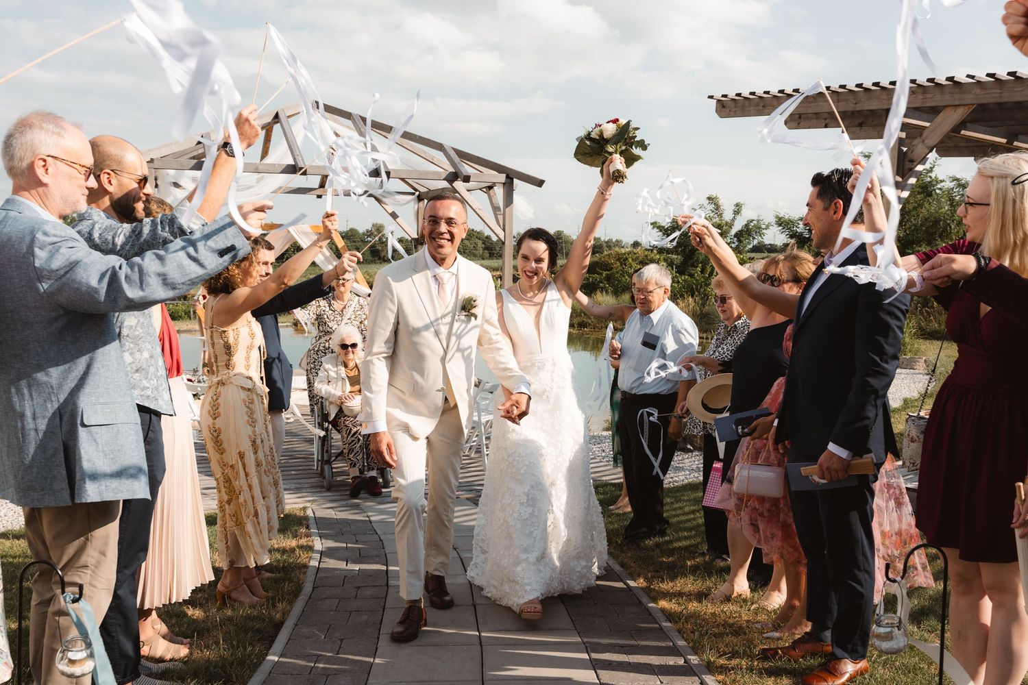Newlyweds walking through ribbon arch as guests celebrate their outdoor wedding ceremony exit.