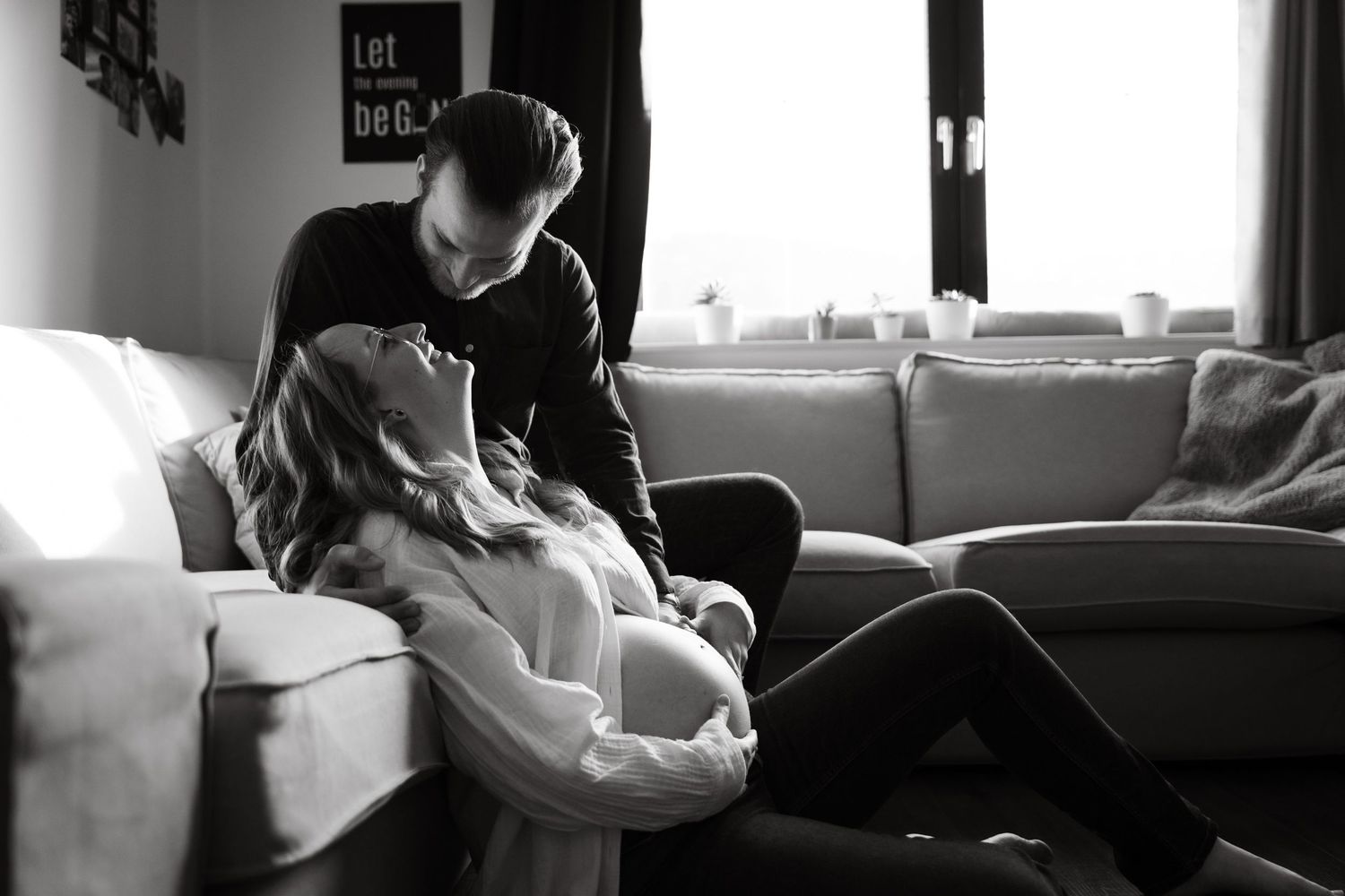 Black and white photo of a couple sharing a tender moment on a couch during pregnancy.