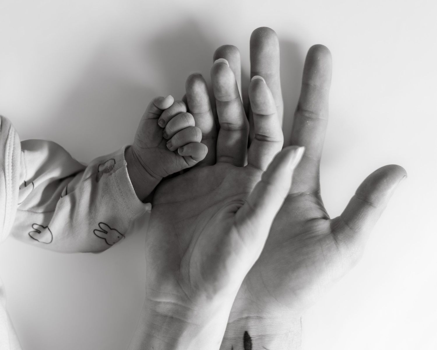 Black and white photo of a newborn baby's tiny hand gripping an adult's finger.