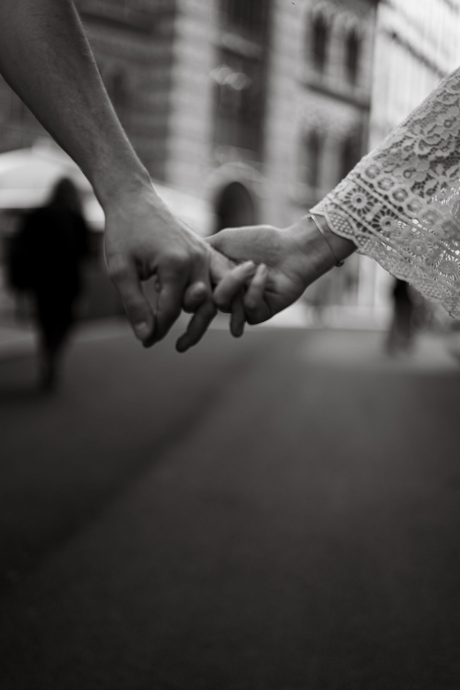 Black and white close-up of couple holding hands while walking on a city street.