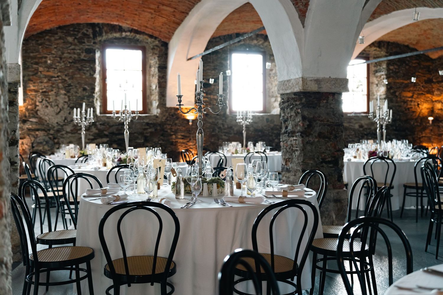 Elegant wedding reception in rustic stone venue with round tables and candelabras.