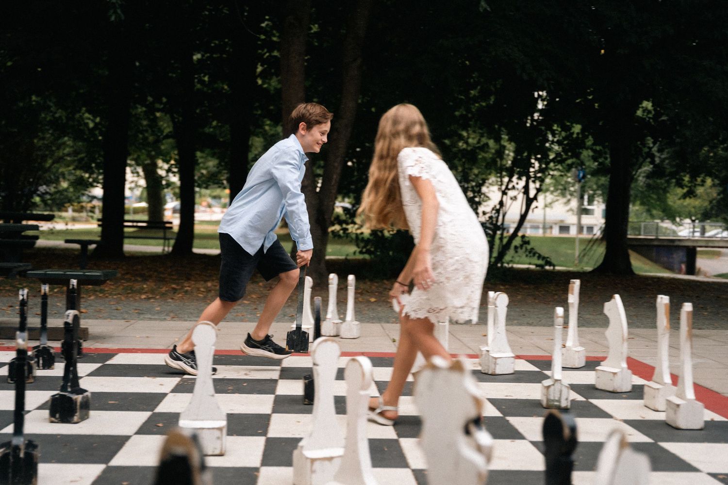 Two teenagers playing on a giant outdoor chess board in a park.