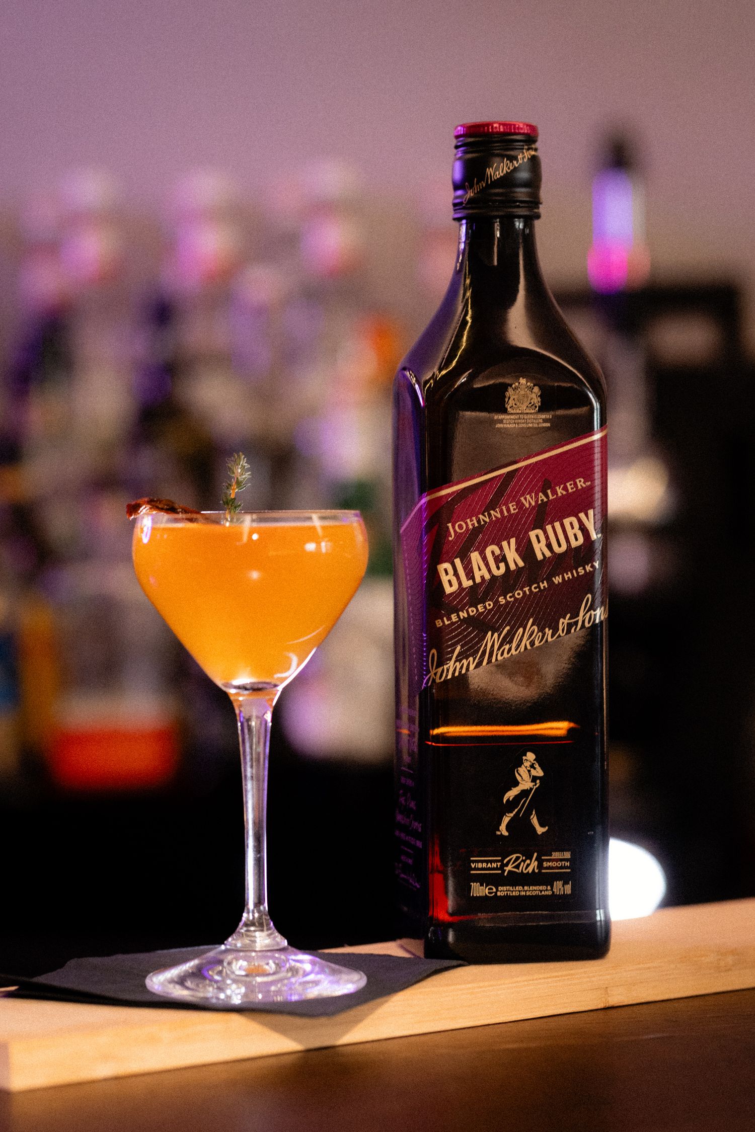 Johnnie Walker Black Ruby Scotch whisky bottle next to an elegant orange cocktail in a coupe glass.